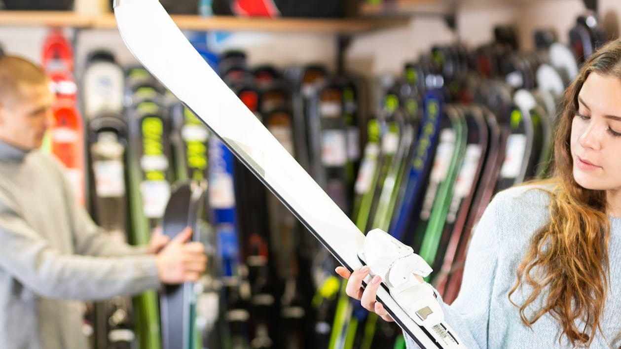 A woman picks up a ski in a ski store and looks at it. 