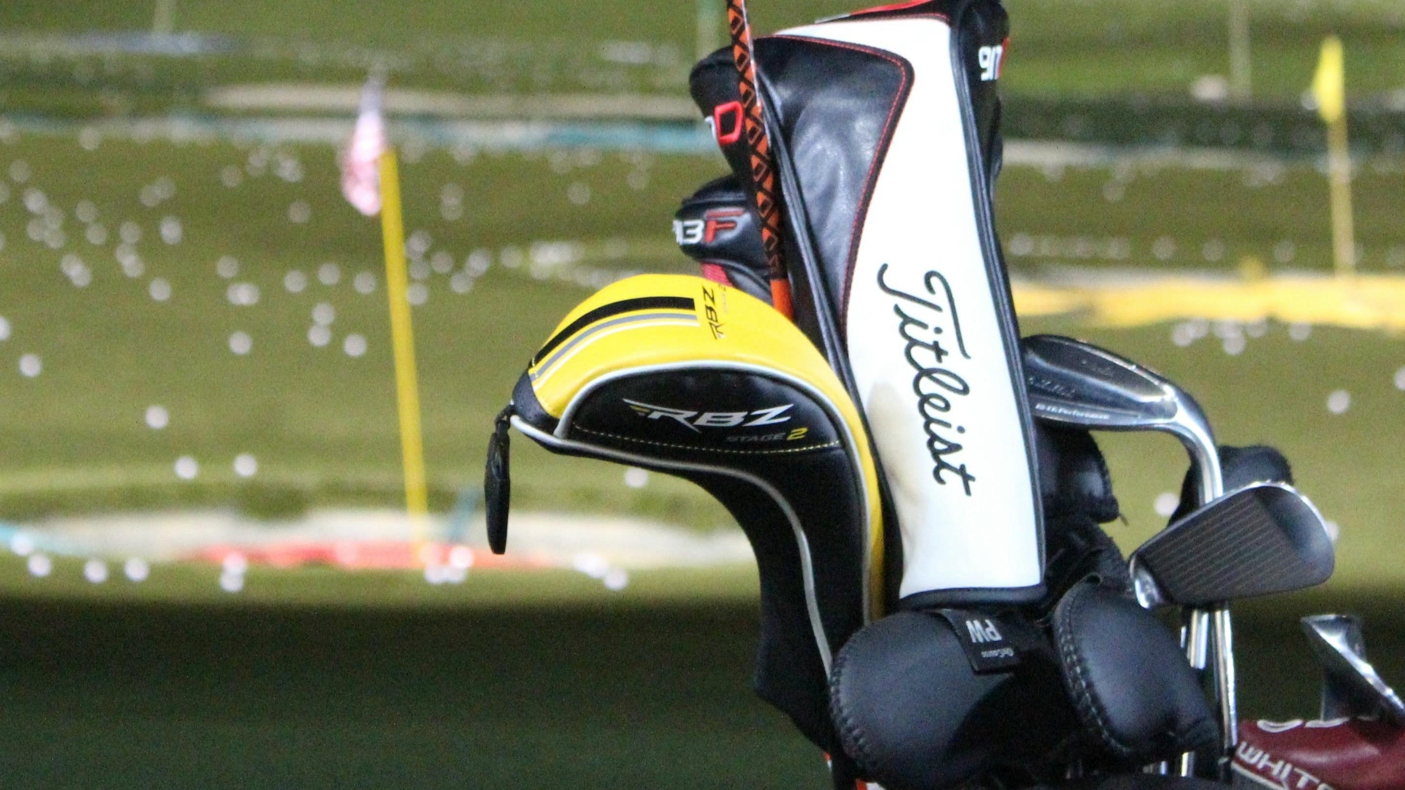 A bag of golf clubs with a driving range in the background. 