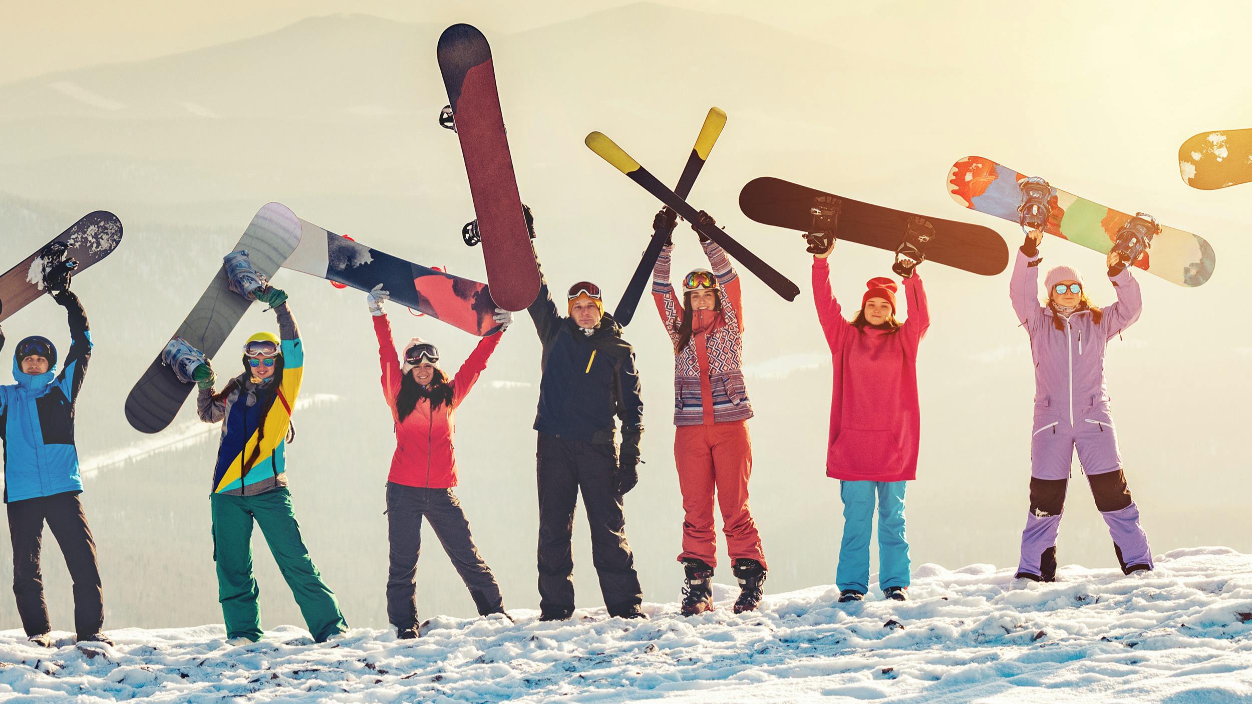 Several snowboarders holding their boards up at the top of a snowy mountain. 