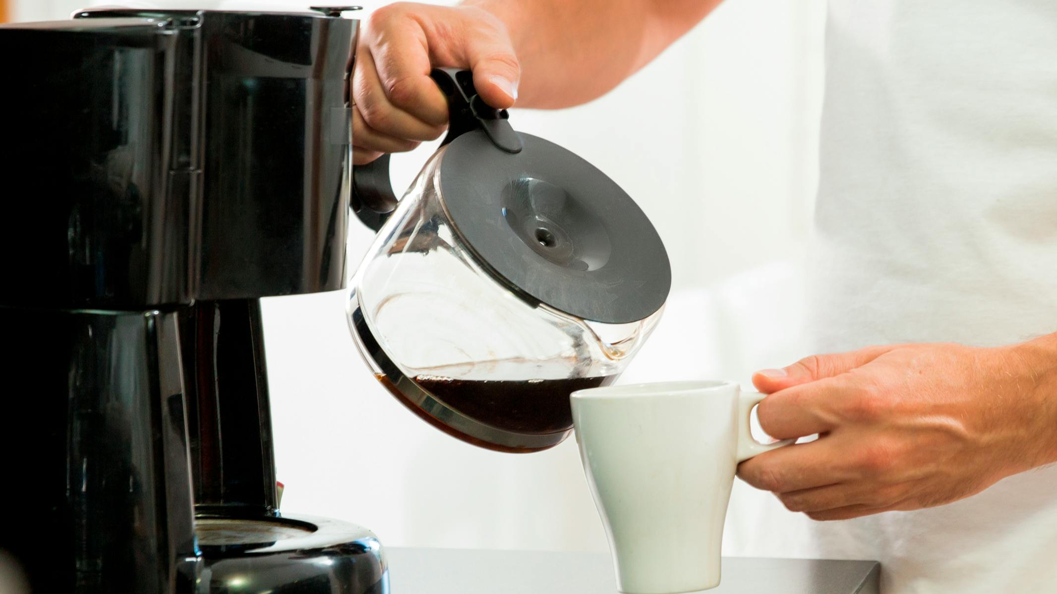 Man in the kitchen pouring a mug of hot filtered coffee from a glass pot.