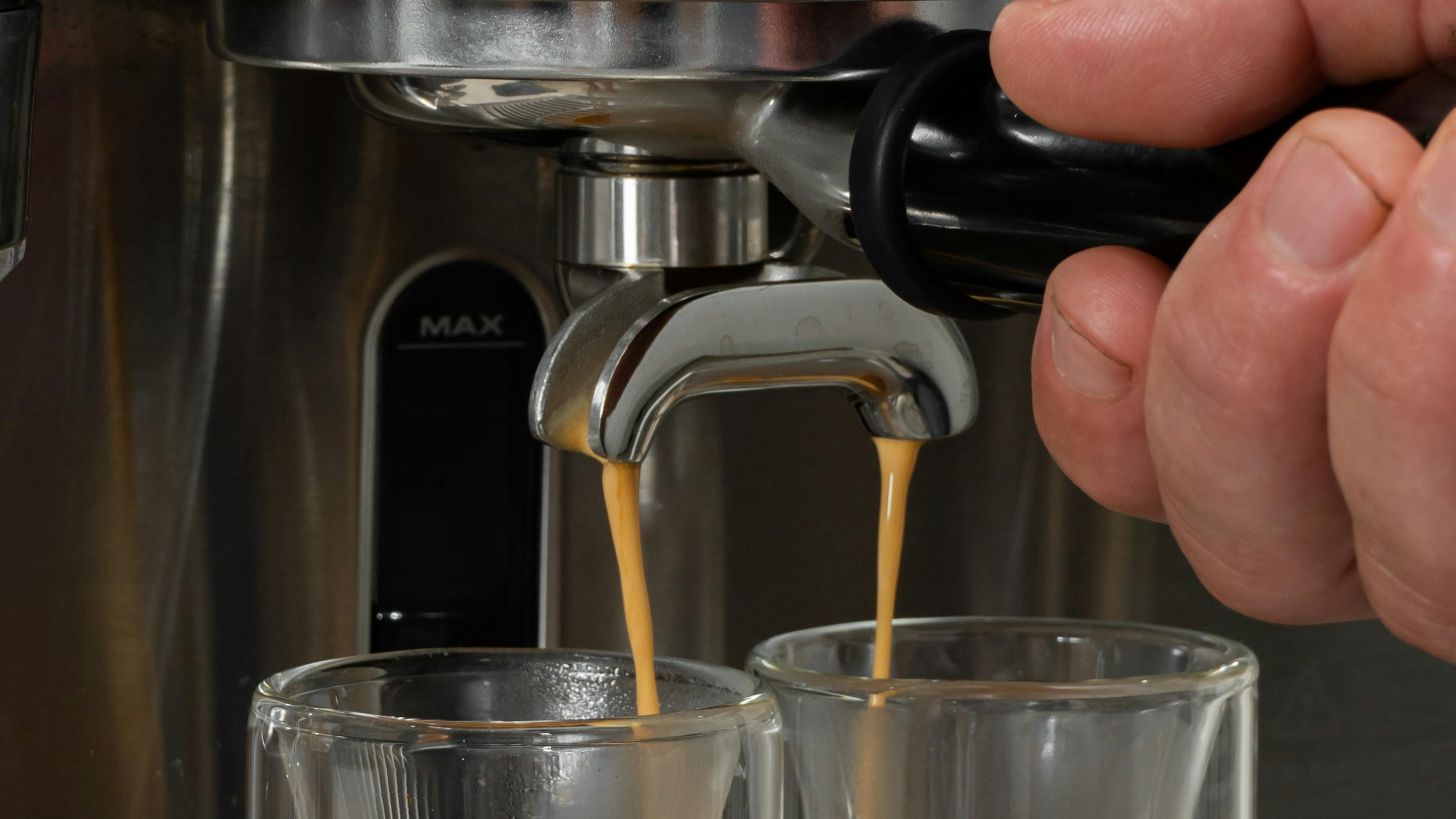 A hand operating an espresso machine as it pours espresso into two cups. 