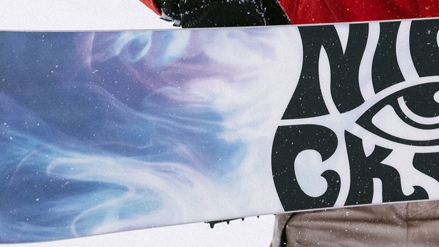 A snowboarder holding his snowboard with the base side out. The base reads "Nidecker".