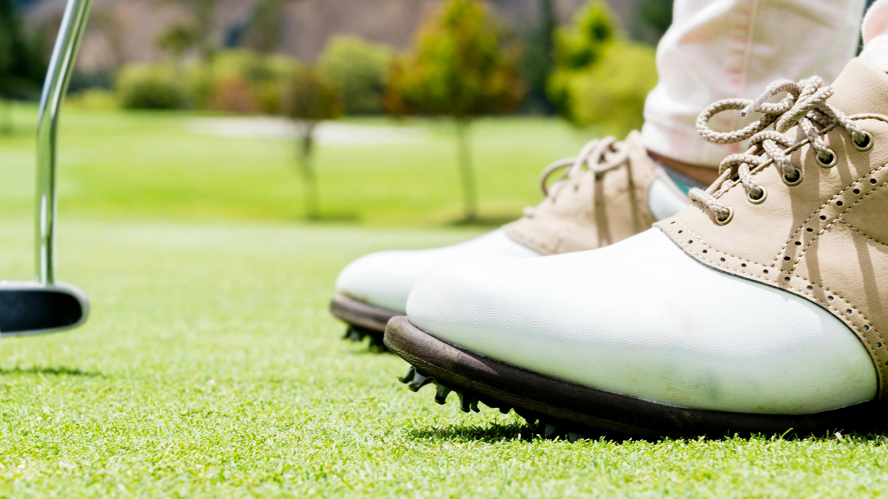 A golfer shoes as he stands on a course. He is putting a white golf ball. 