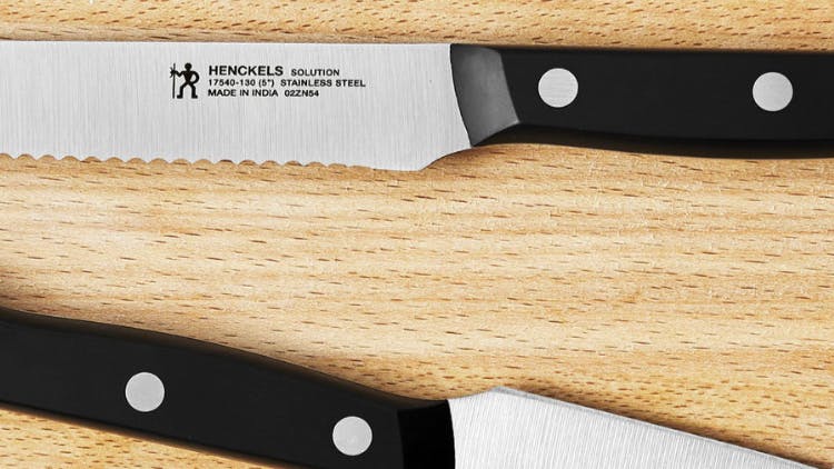 Two Henckels knives laying on a wooden cutting board. 