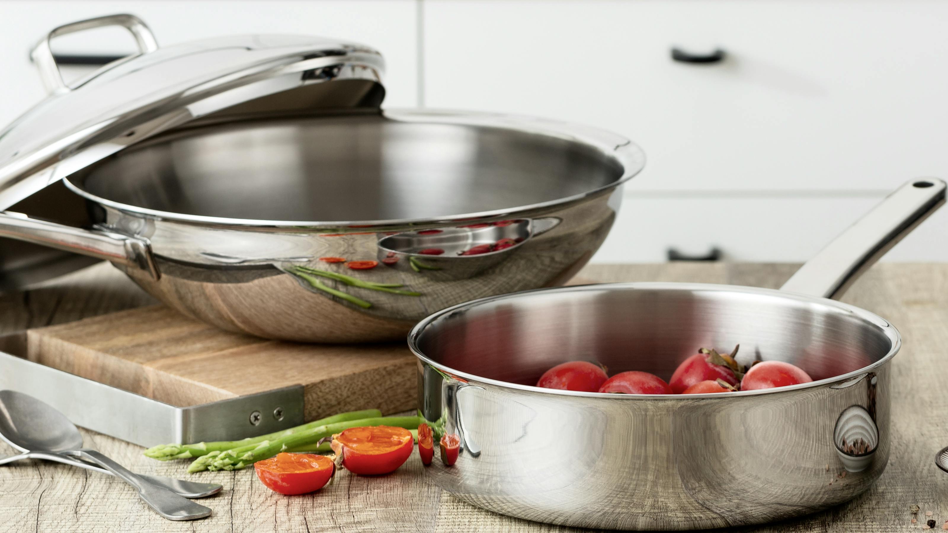 Two stainless steel pans on a countertop with food in them. There are some vegetables next to the pans. 