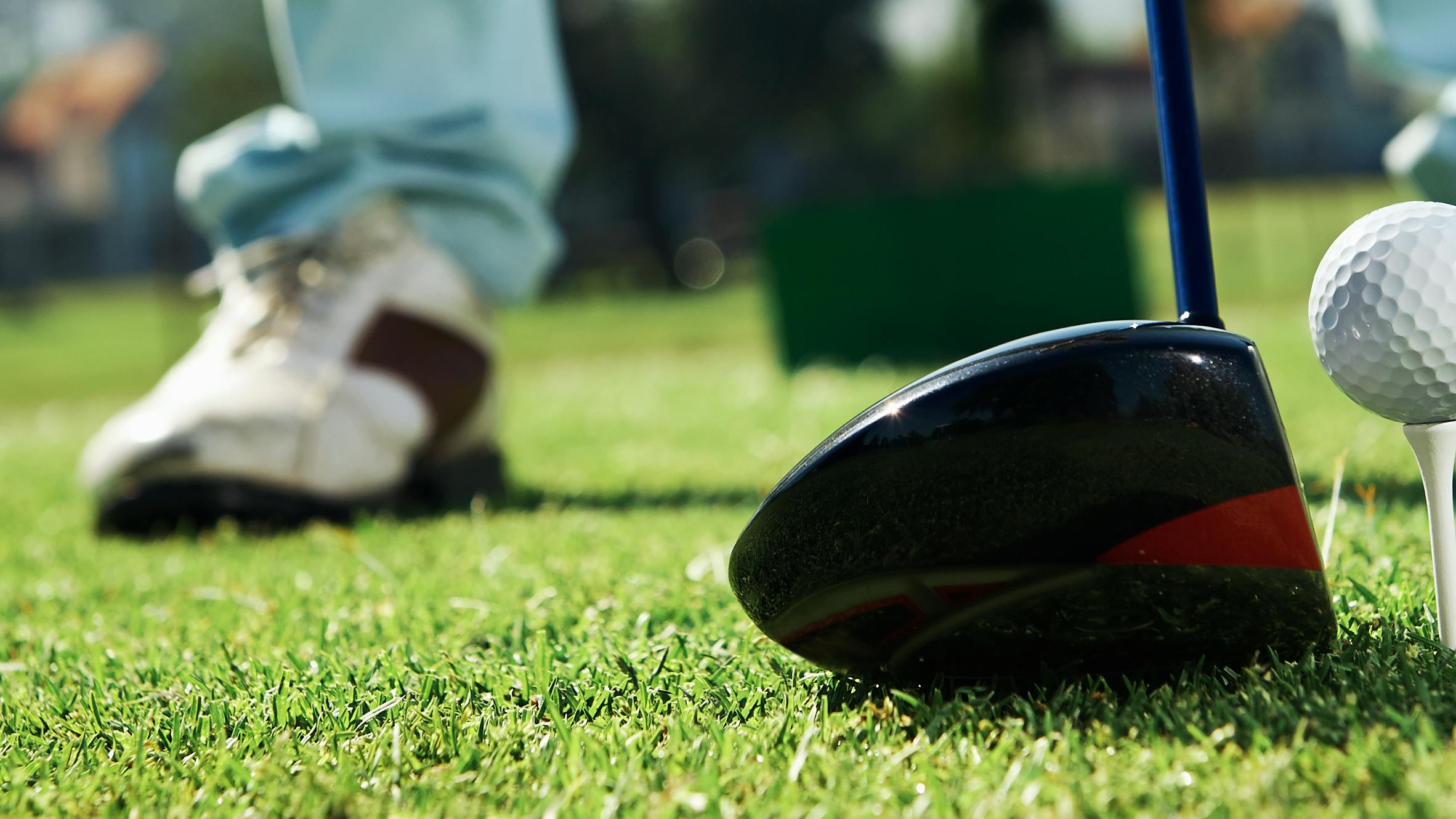 Close up of a golf driver with a teed up golf ball in front of it. 