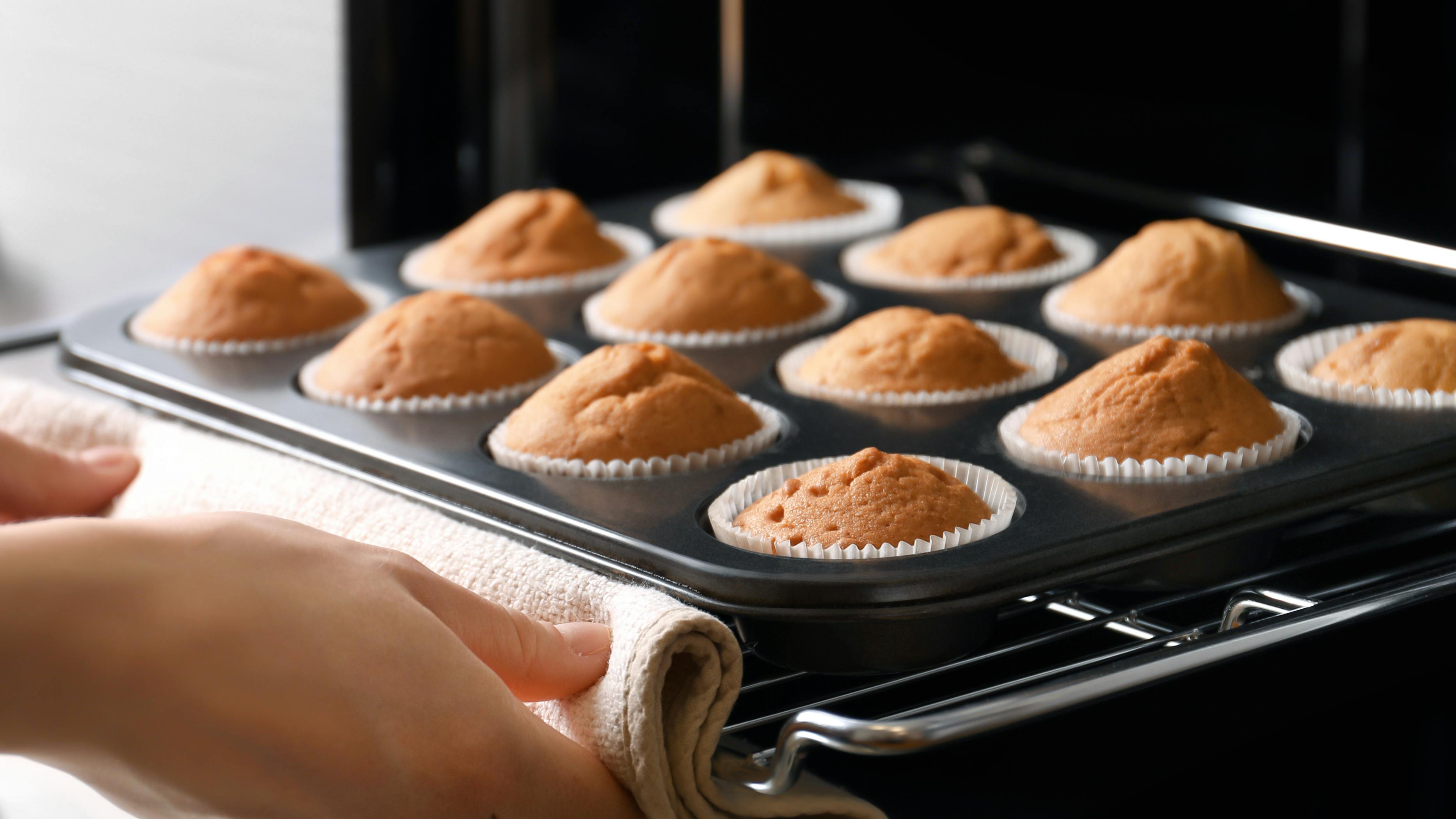A woman taking muffins out of an oven. 