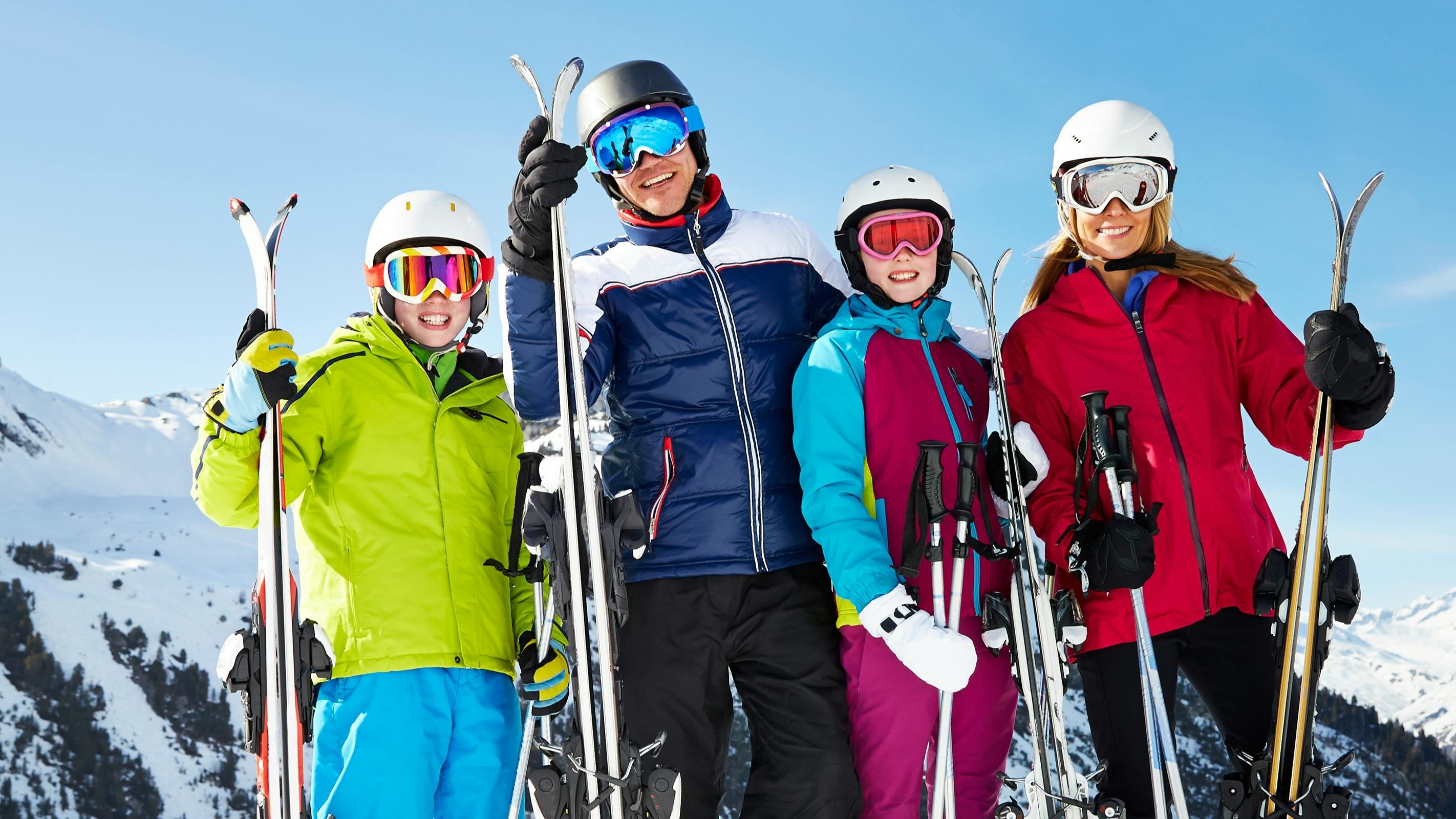 Four skiers standing at the top of a snowy mountain while holding their skis. 