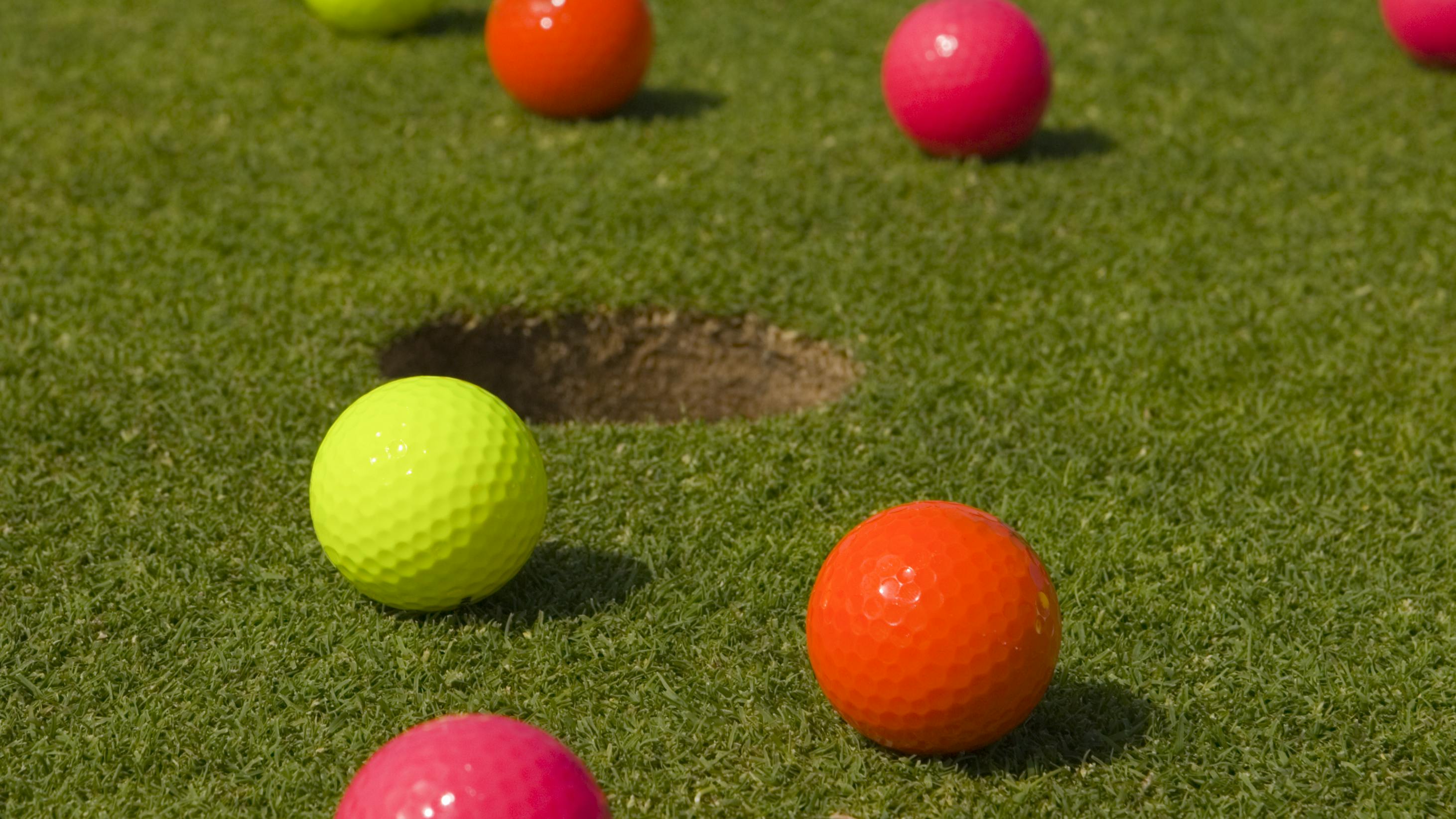 Bright golf balls sitting around a hole. 