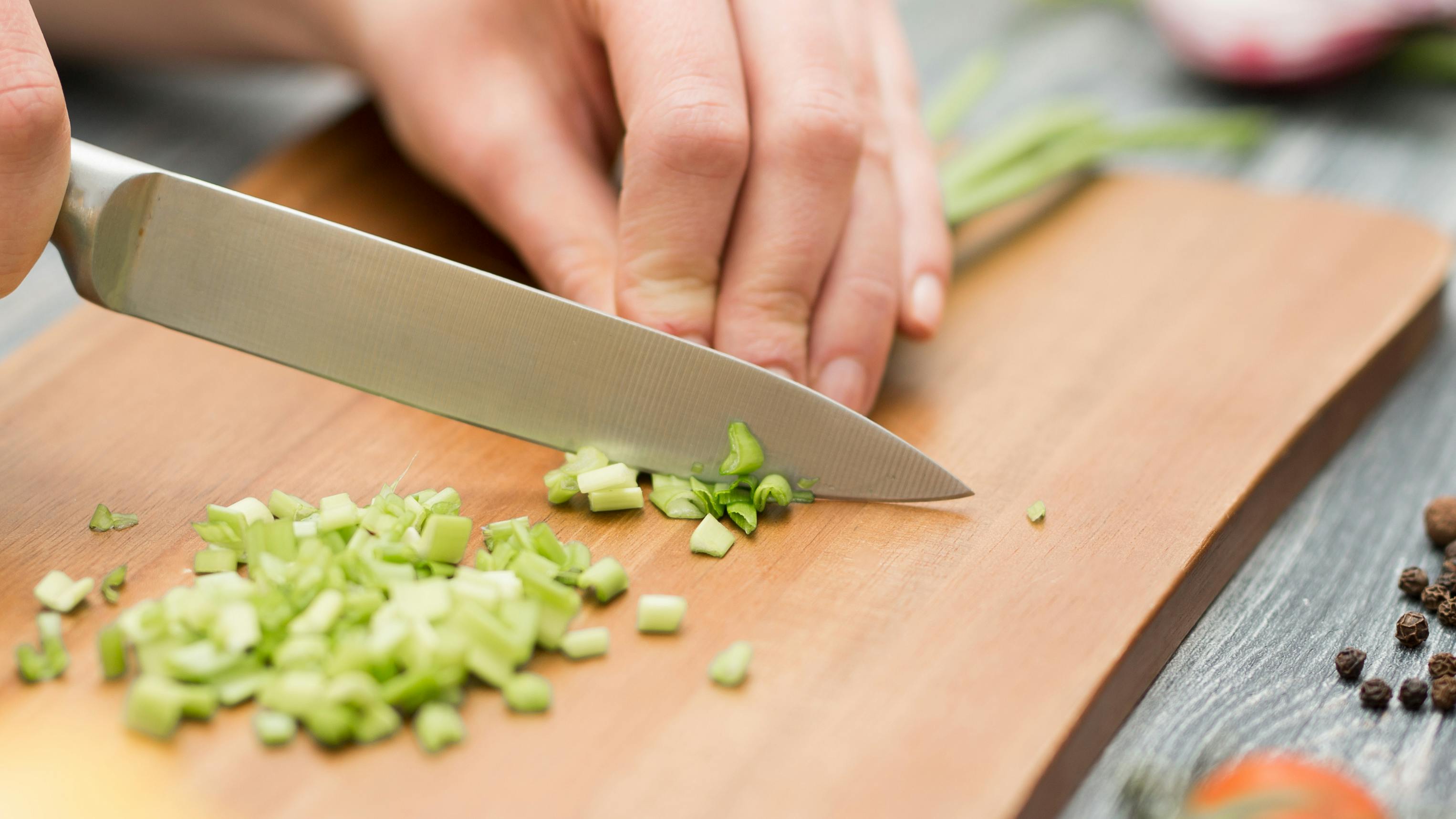 Close up of someone chopping green onions on a cutting board.