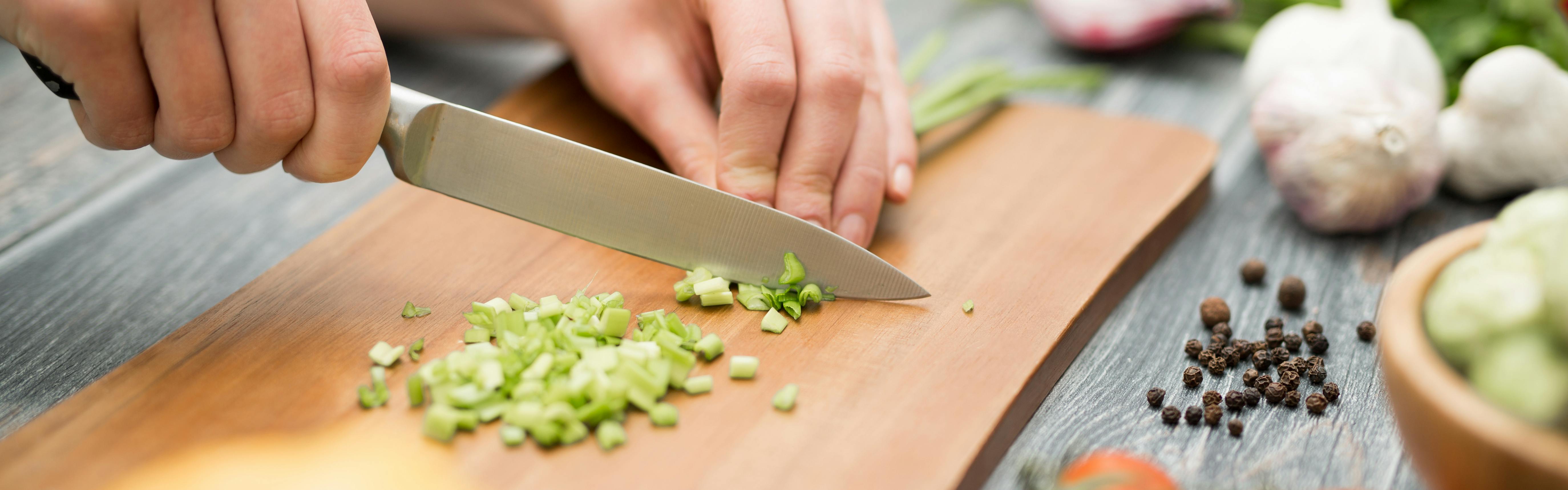 Close up of someone chopping green onions on a cutting board.