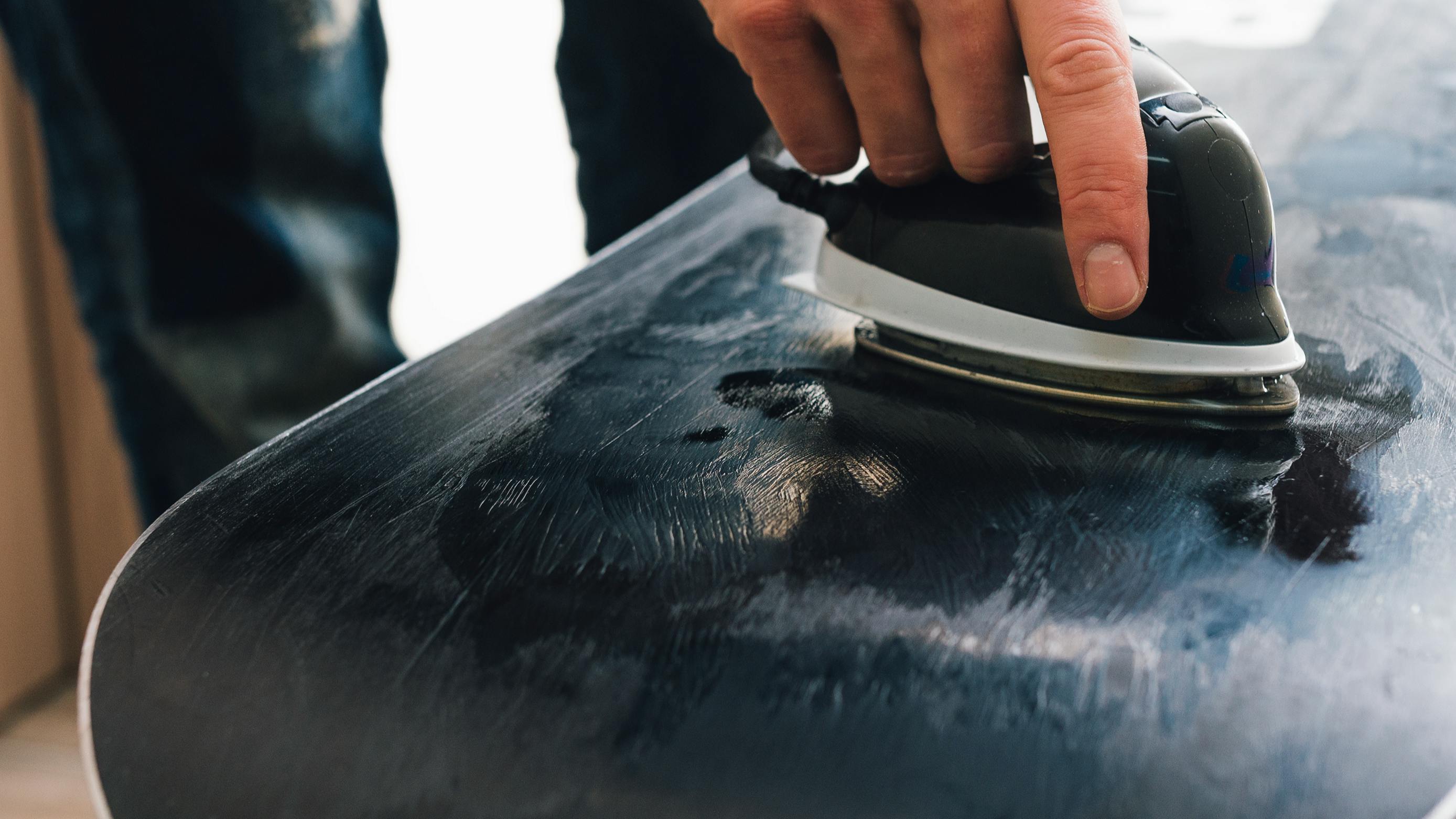 A snowboarder waxes the base of his snowboard. 