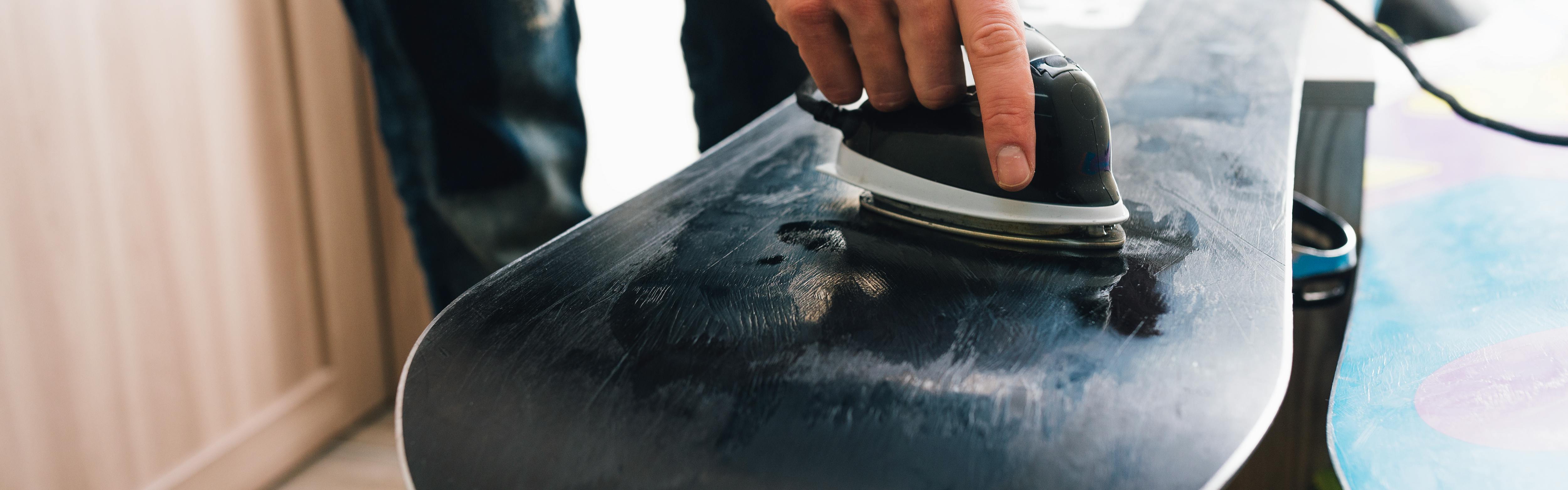 A snowboarder waxes the base of his snowboard. 