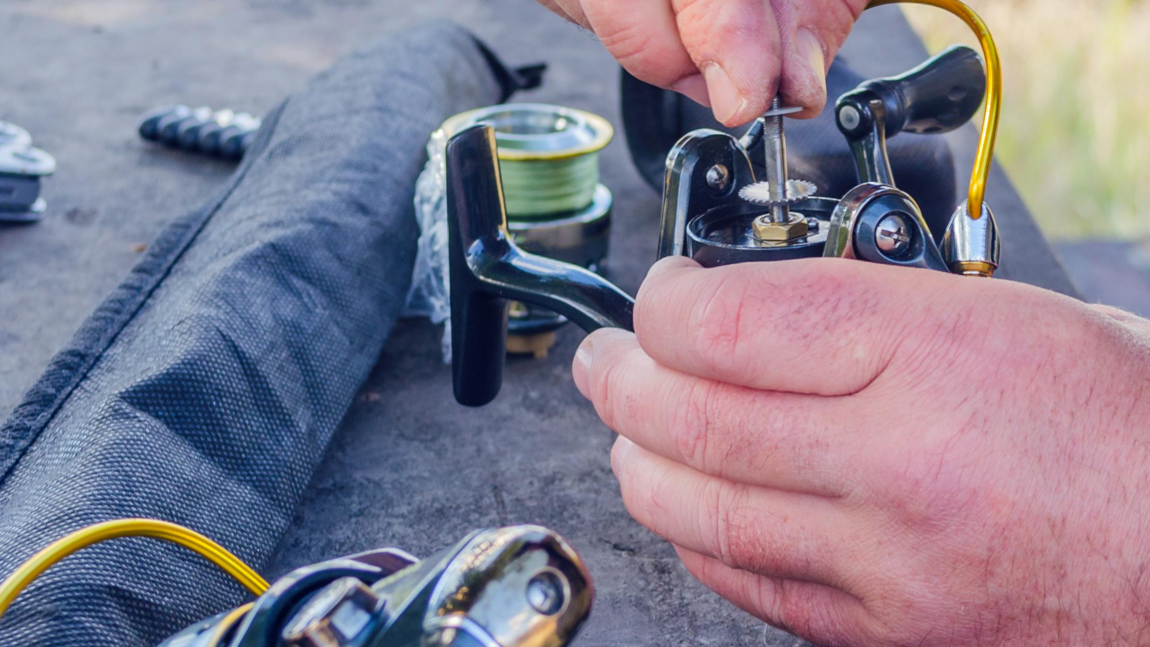 Hands working on a fishing reel.