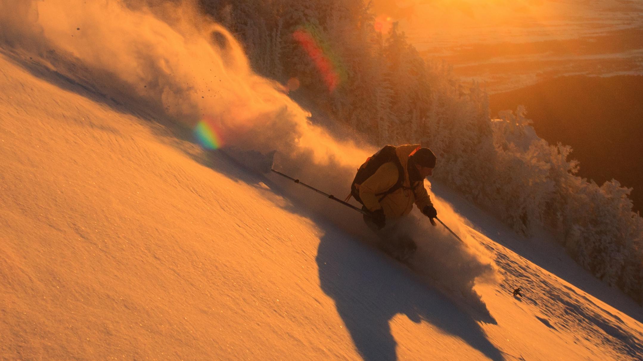 A skier turns down a snowy mountain as the sun sets. 