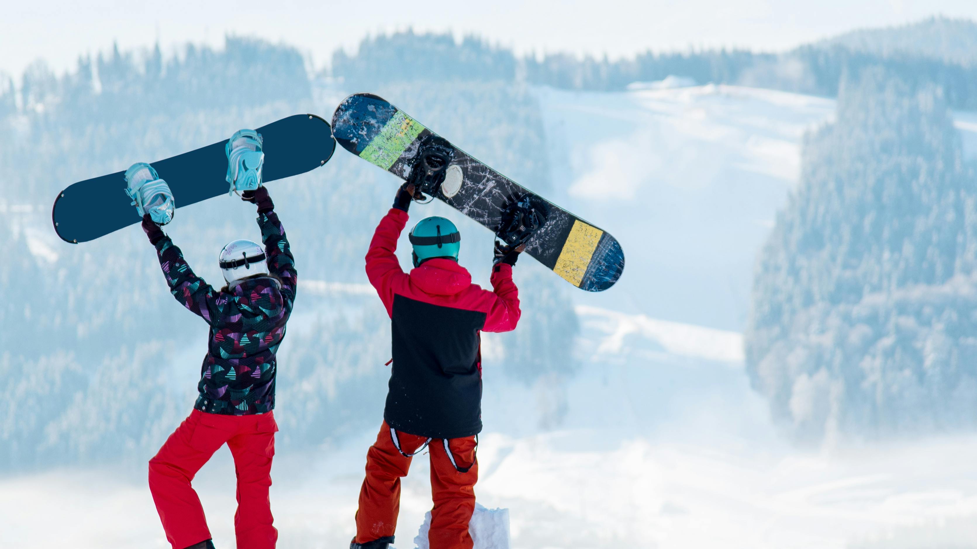 Two snowboarders sitting next to each other as they hold their snowboards in the air. 