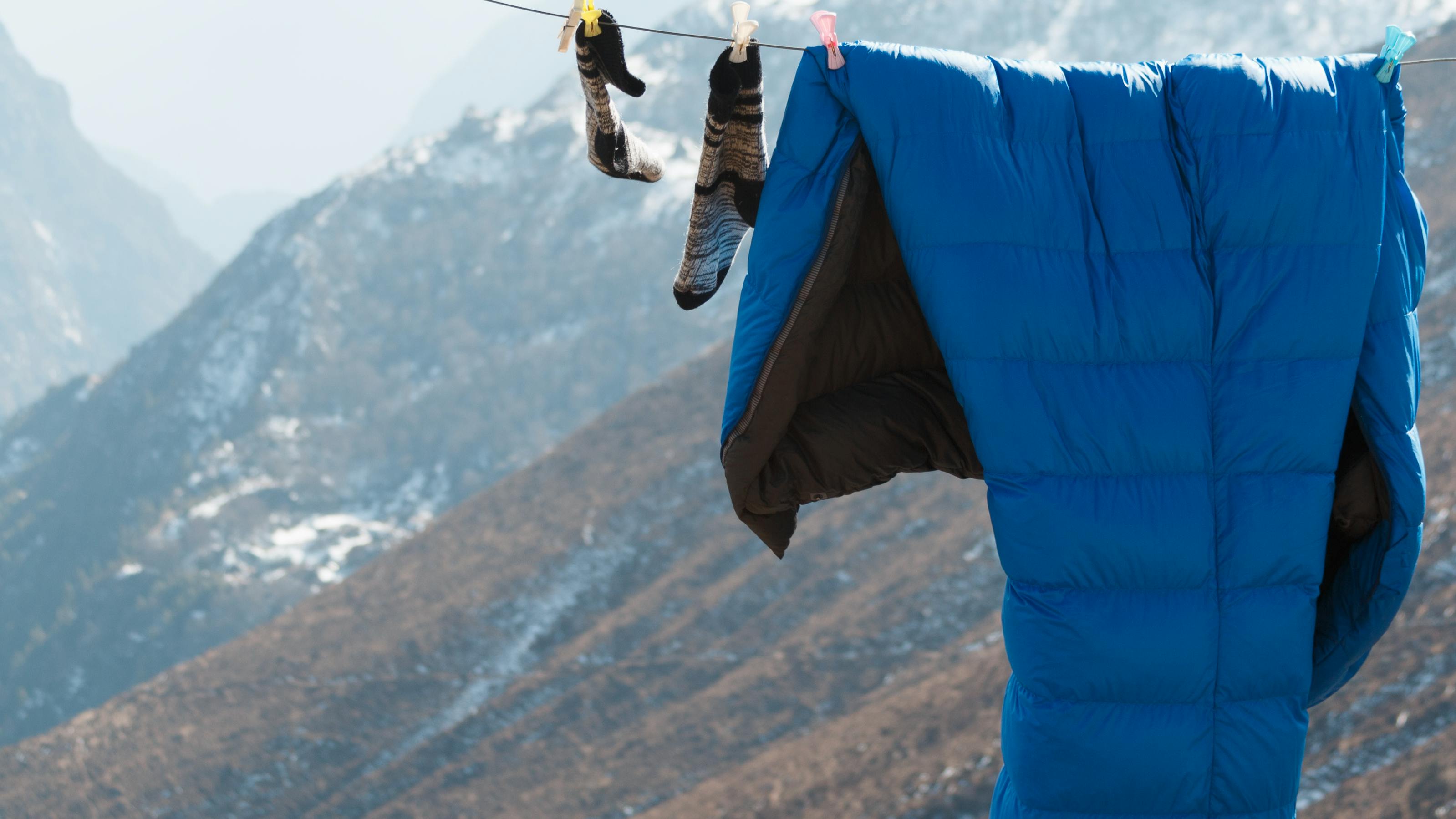 A sleeping bag hanging on a drying like with mountains in the background. 