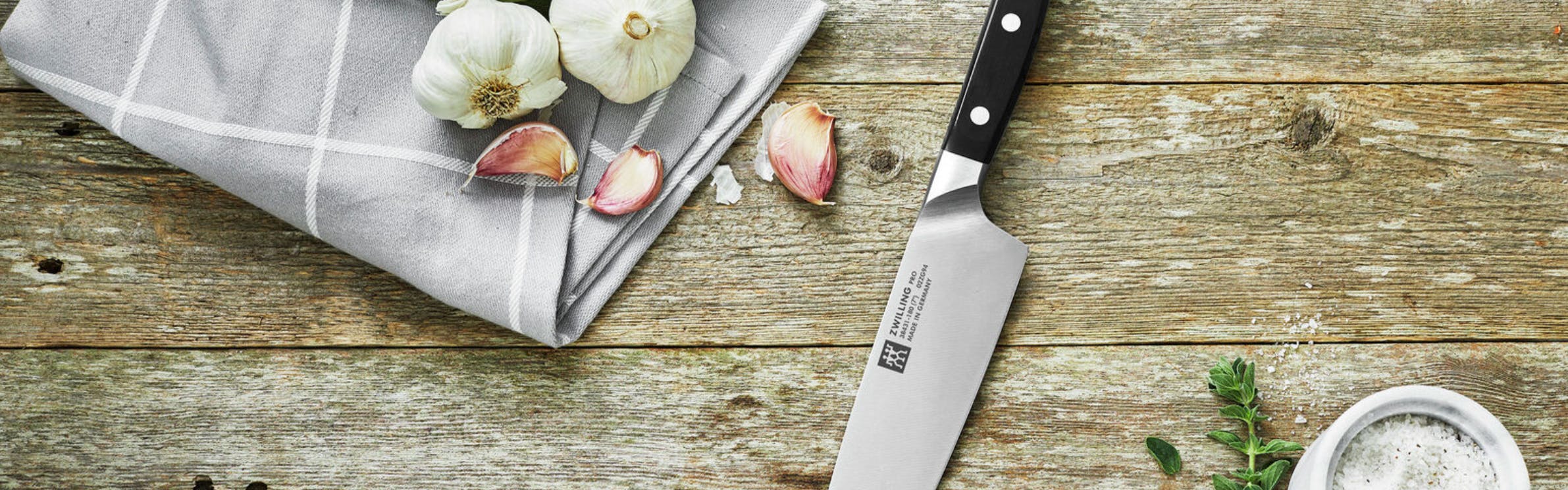 A Zwilling knife laying on a table next to some garlic and salt. 