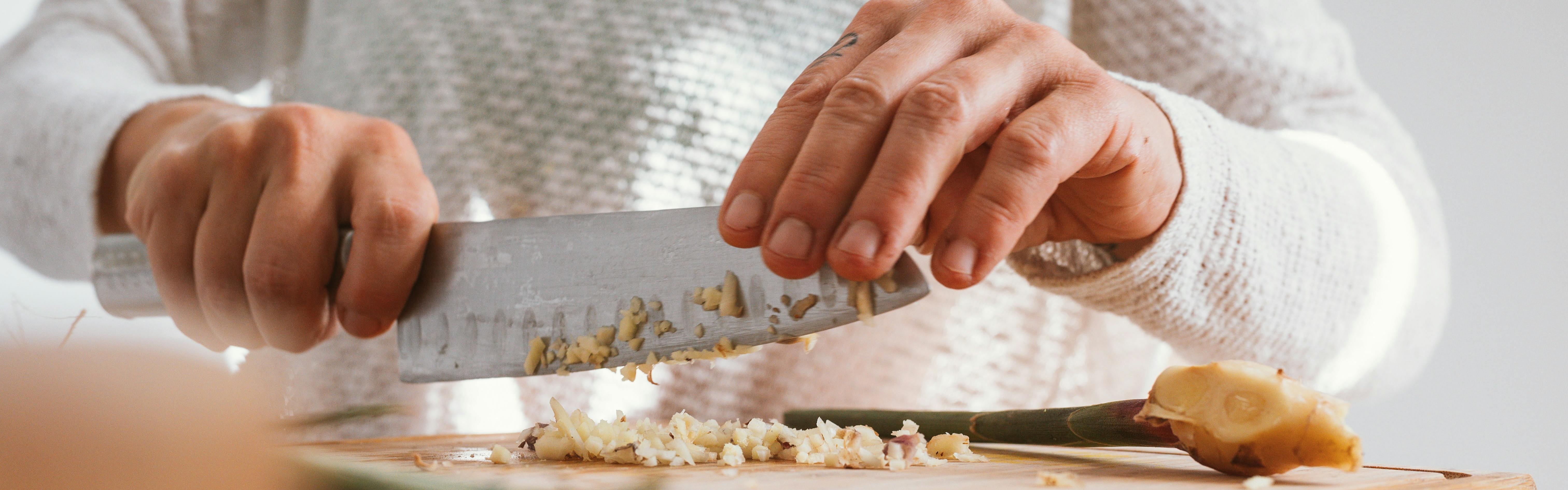 A chef using a knife to chop some garlic.