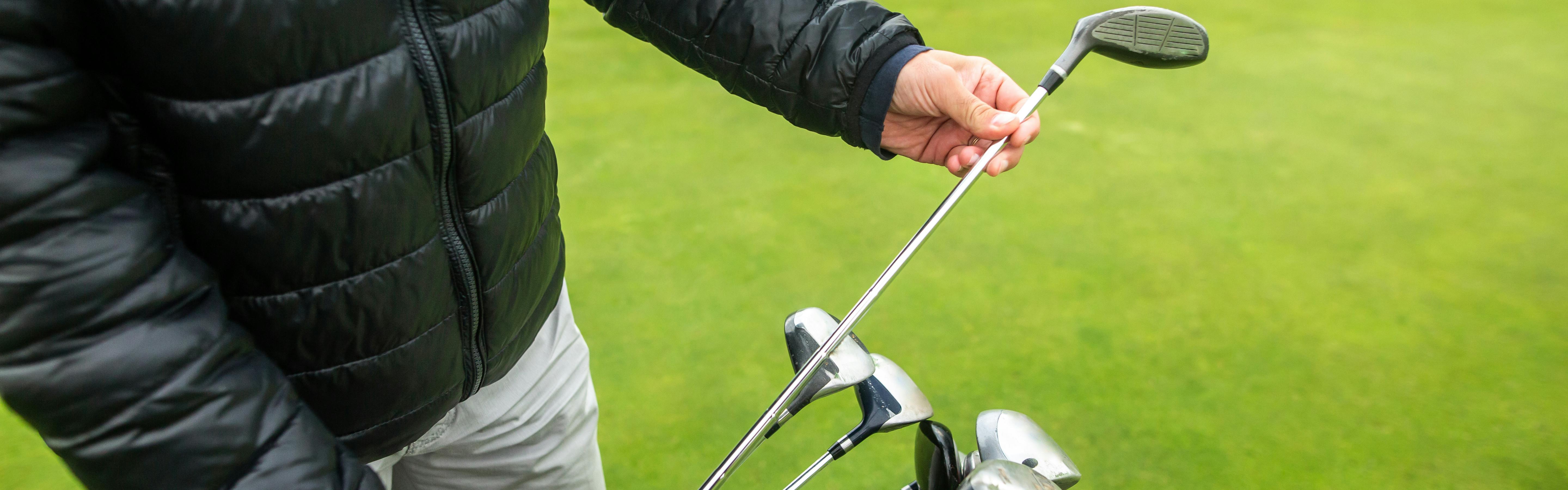 A golfer pulling a club out of his bag as he looks at the shaft. 