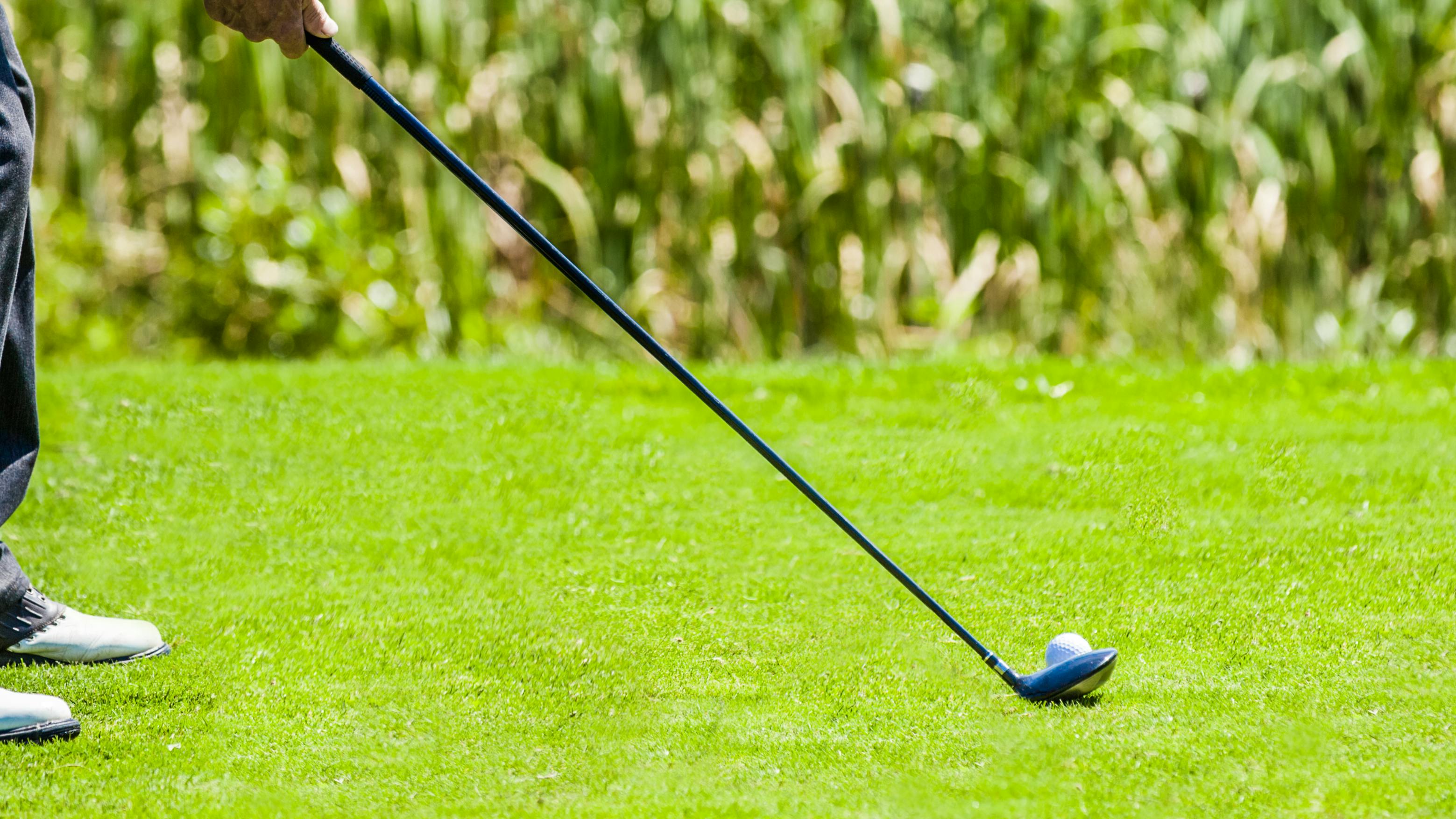 A golfer hitting a golf ball with a hybrid. 