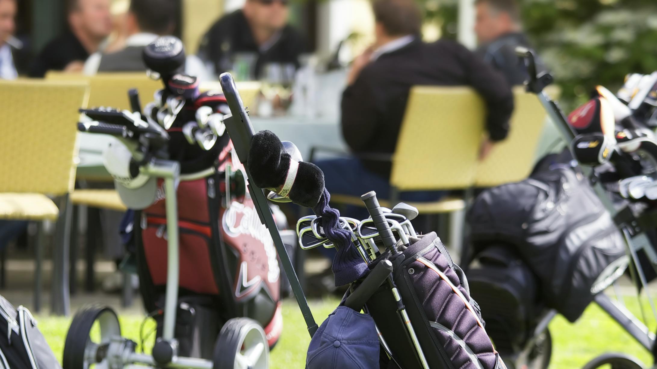 Several golf bags sit together, most of the golf drivers have headcovers on them. 