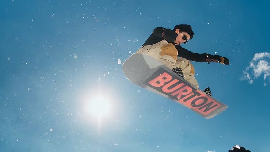 A snowboarder going off a jump on his Burton Snowboard. 