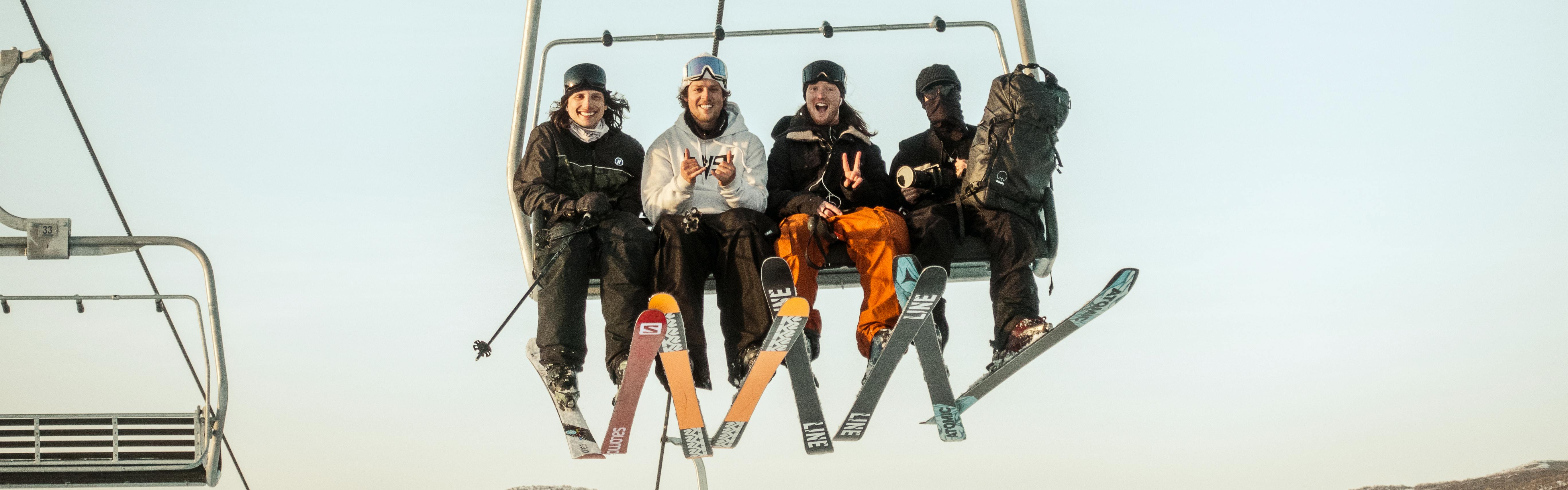 Four skiers on a chairlift all wearing different skis. 