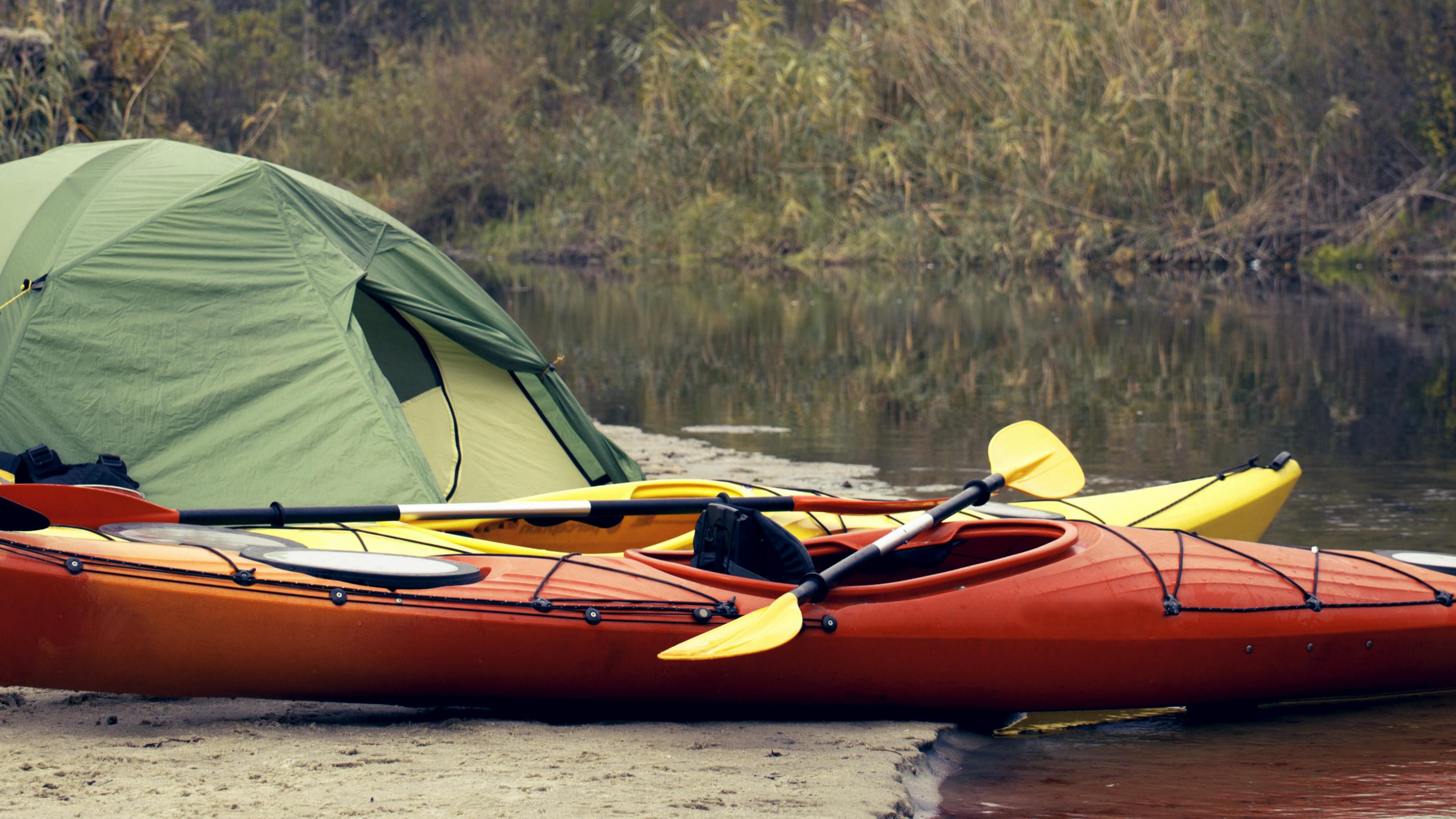 A kayak on the shore next to a green tent. 