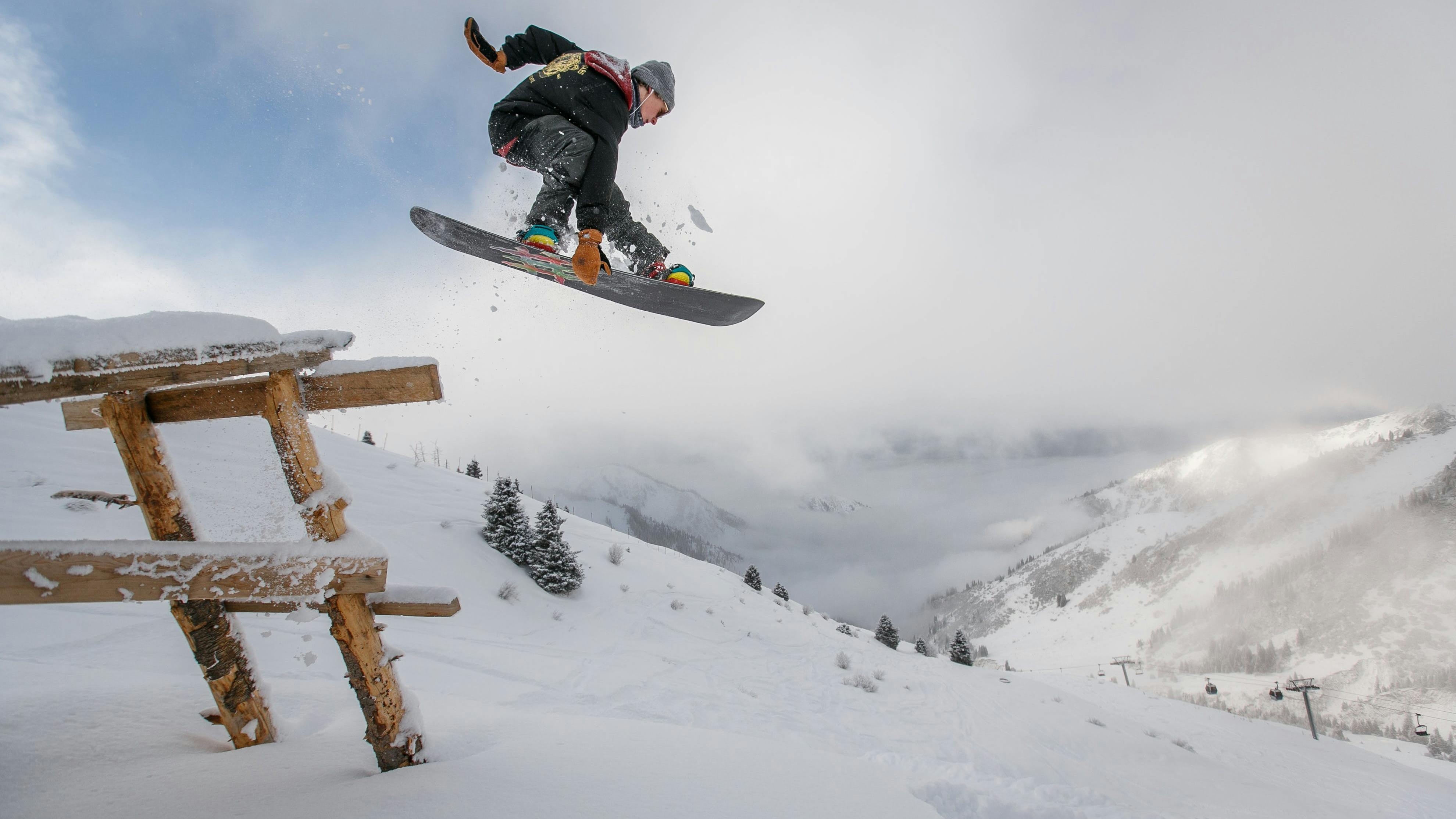 A snowboarder doing a jump off a wooden picnic table. 
