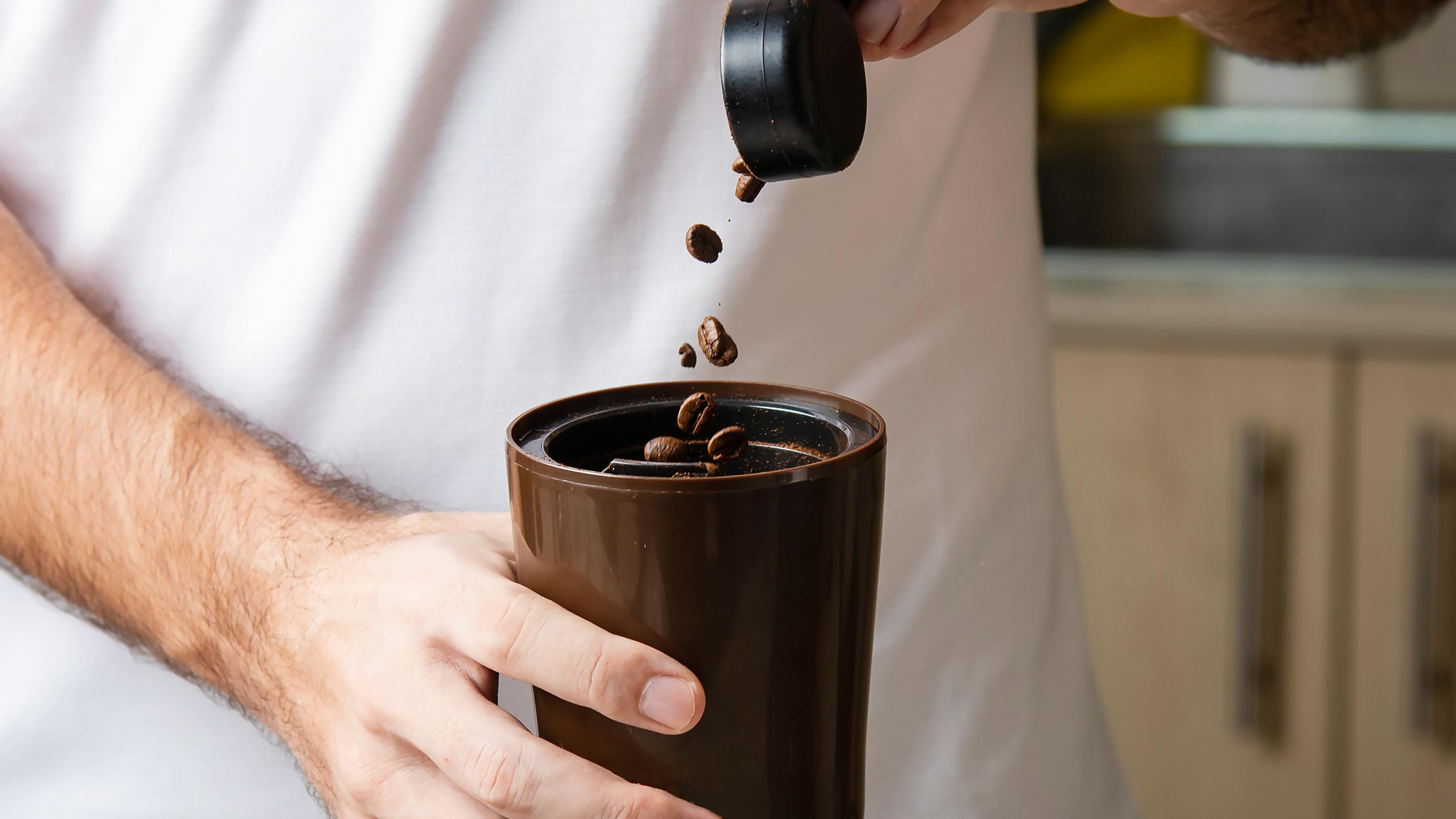 Someone pouring coffee beans into a grinder.