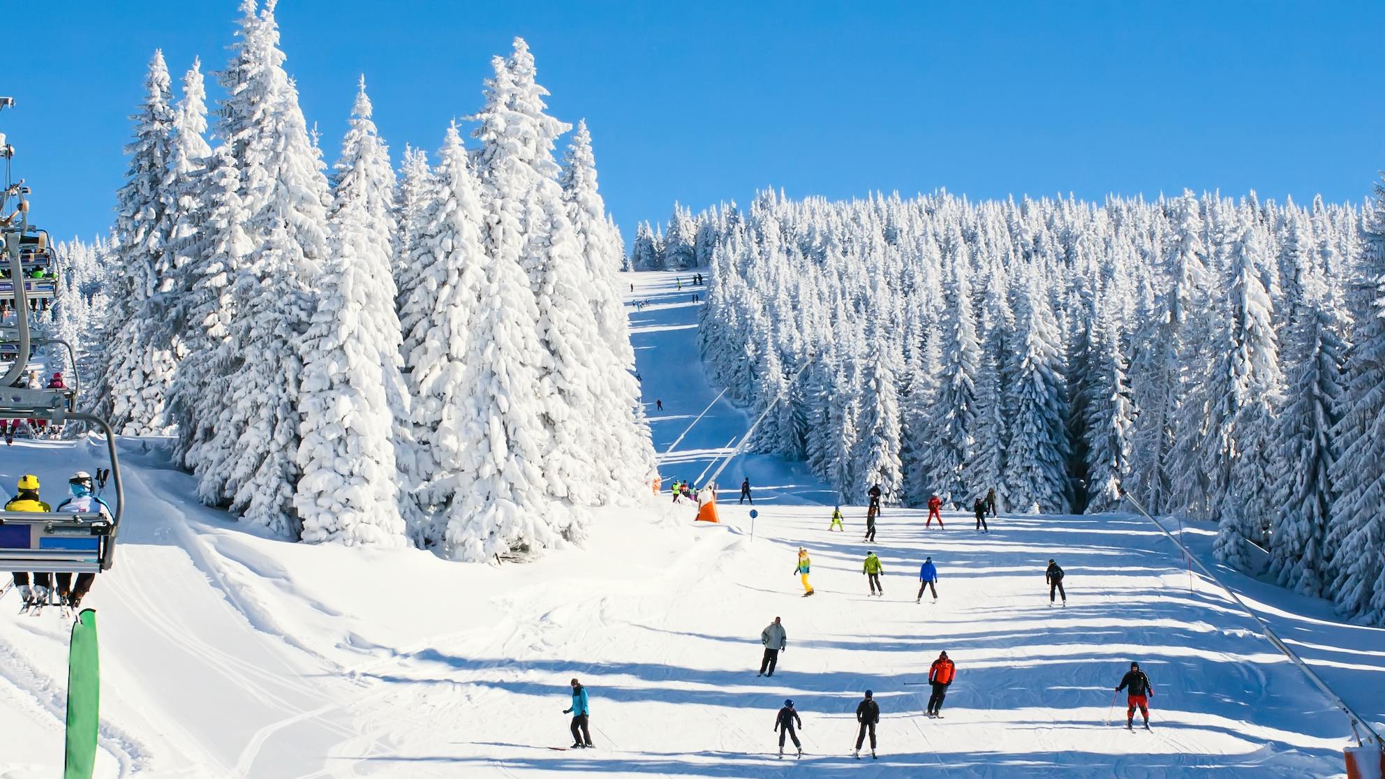 Skiers ride up a lift and ski down a hill at a ski resort.