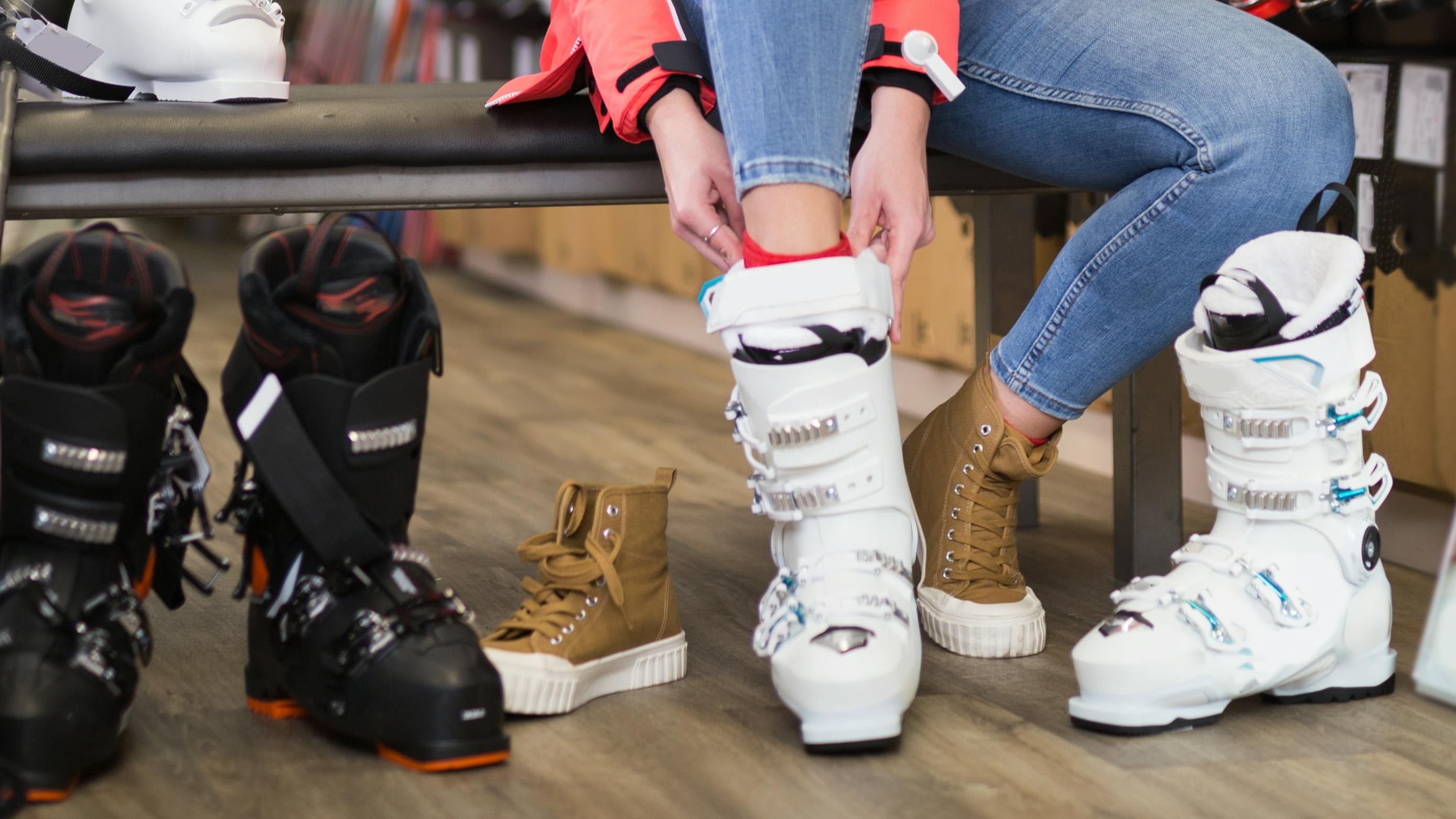 A woman tries on several pairs of ski boots in a store.
