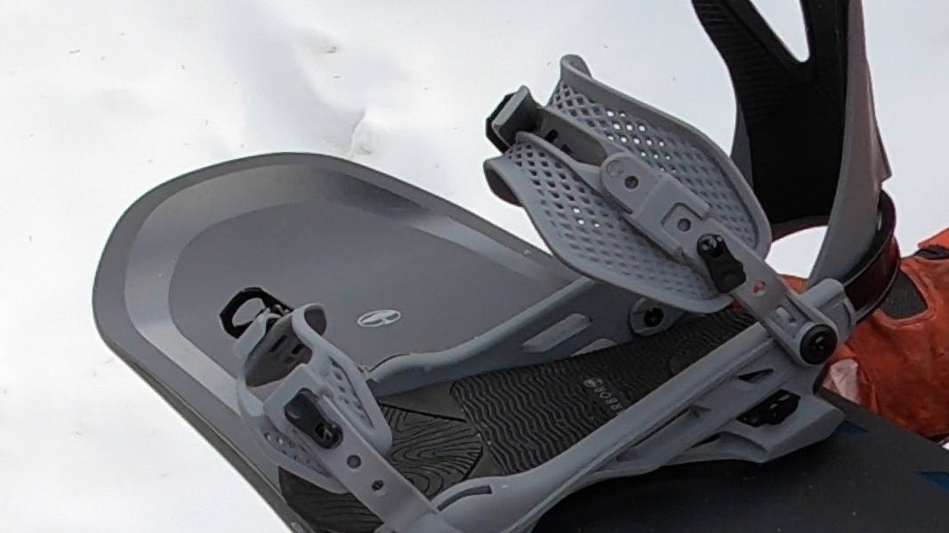 A snowboarder holding a snowboard with the 2024 Arbor Cypress Bindings on them. 