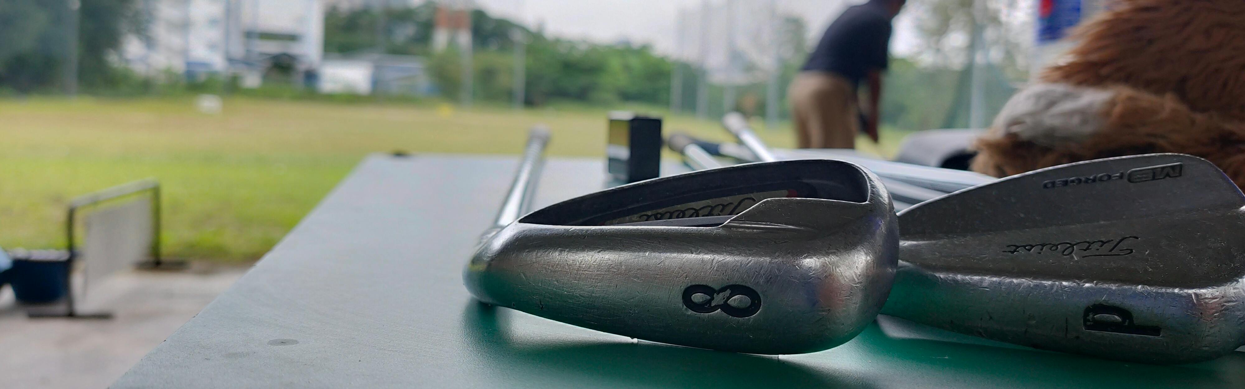 Two Titleist Irons lying on a table at a driving range.