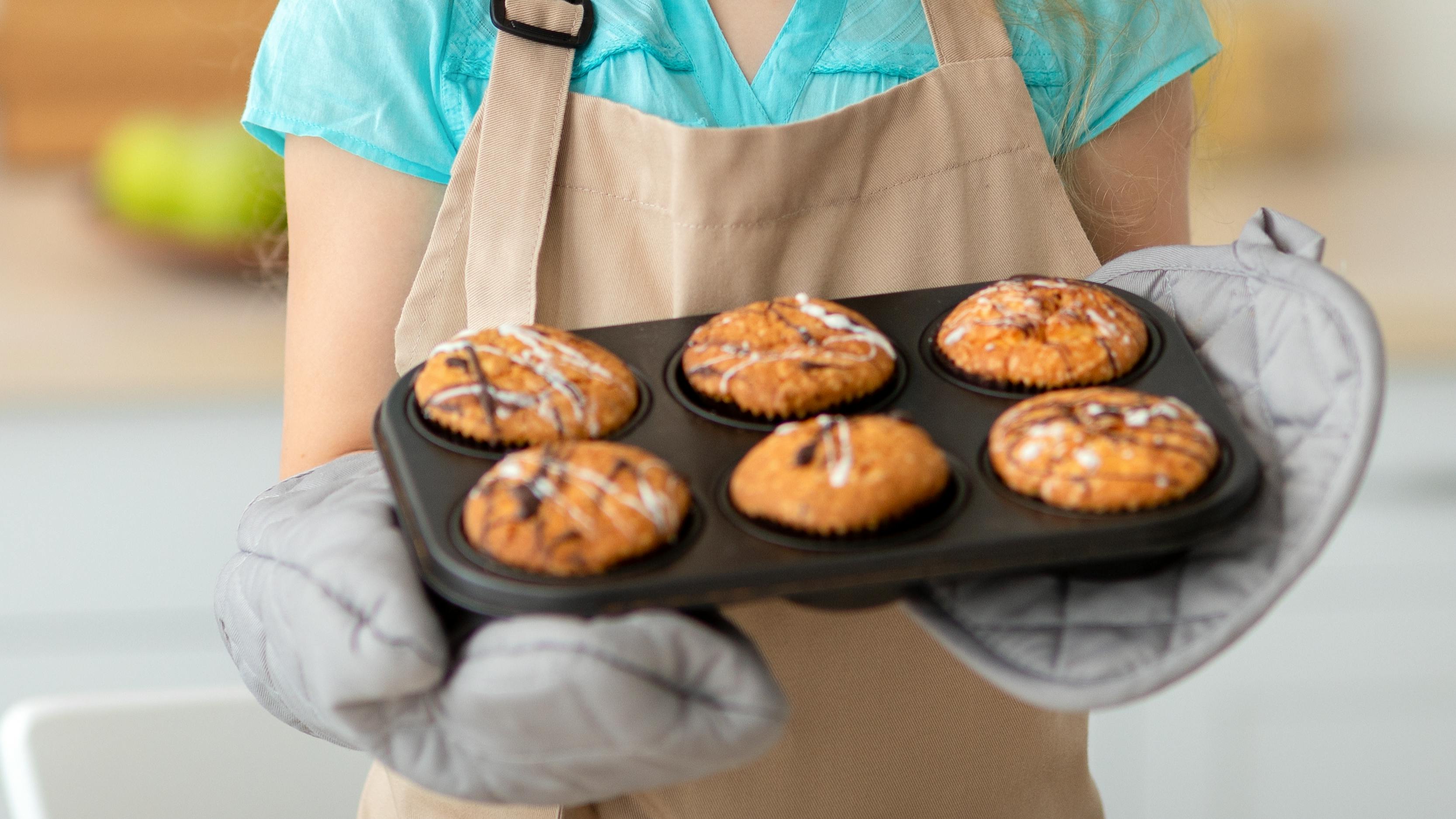 A young girl holding a muffin tin with 6 muffins in it. 
