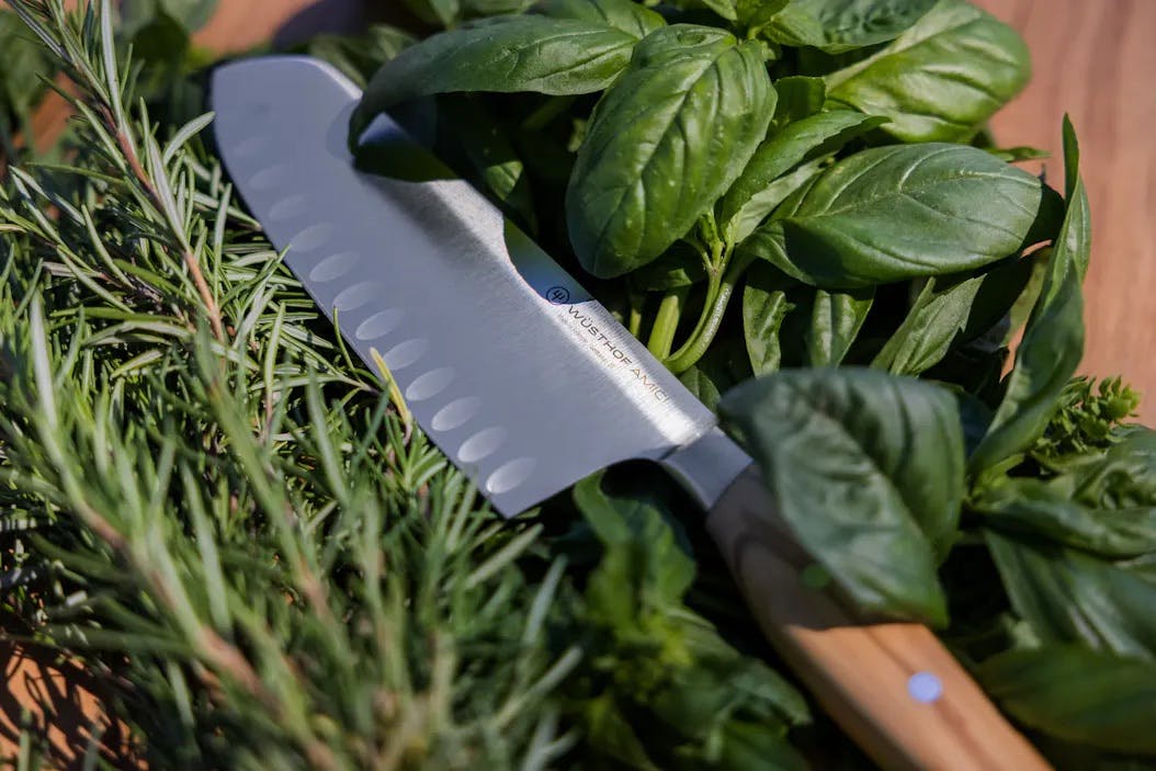A santoku knife nestled in herbs.