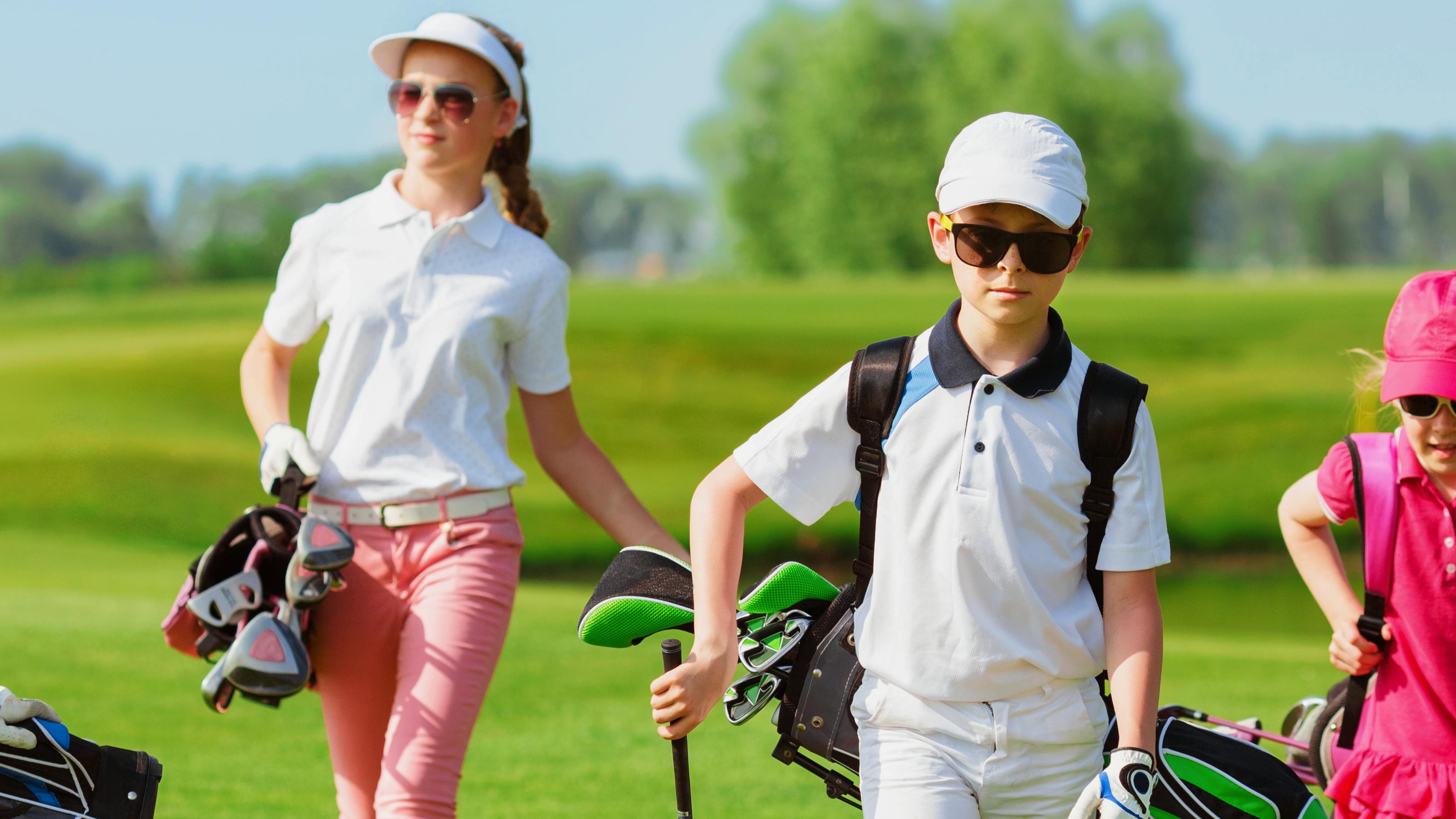Four young golfers walk towards the camera with their golf bags. 