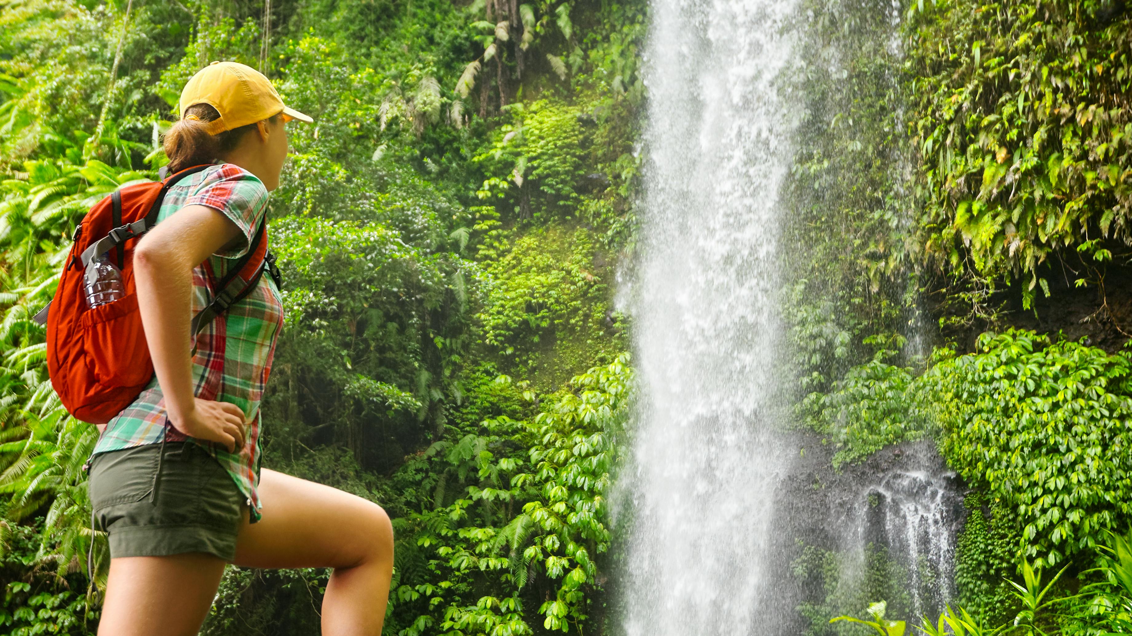 A woman looking at a waterfall as shes wearing a hiking backpack and full hiking gear. 