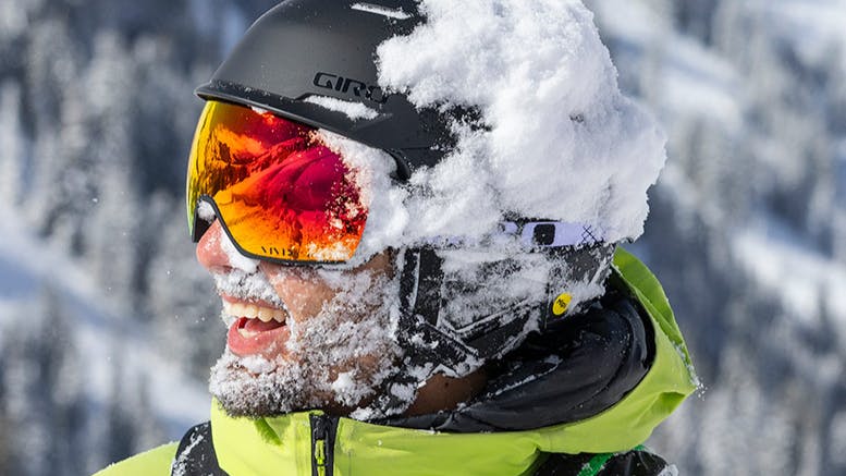 A snowboarder wearing a black Giro helmet with snow piled on one side of it. 