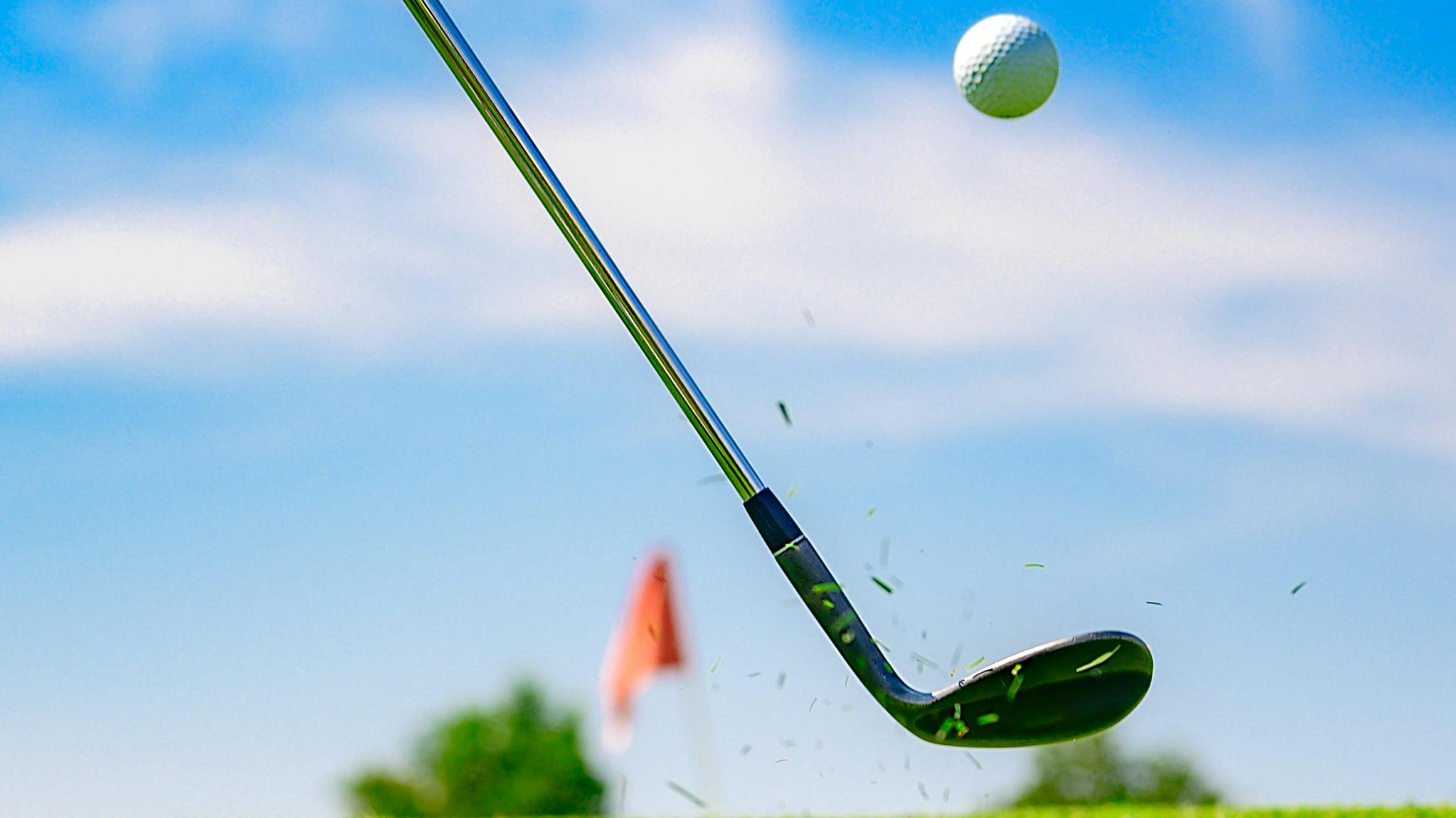 A golfer hitting a golf ball with a wedge. 