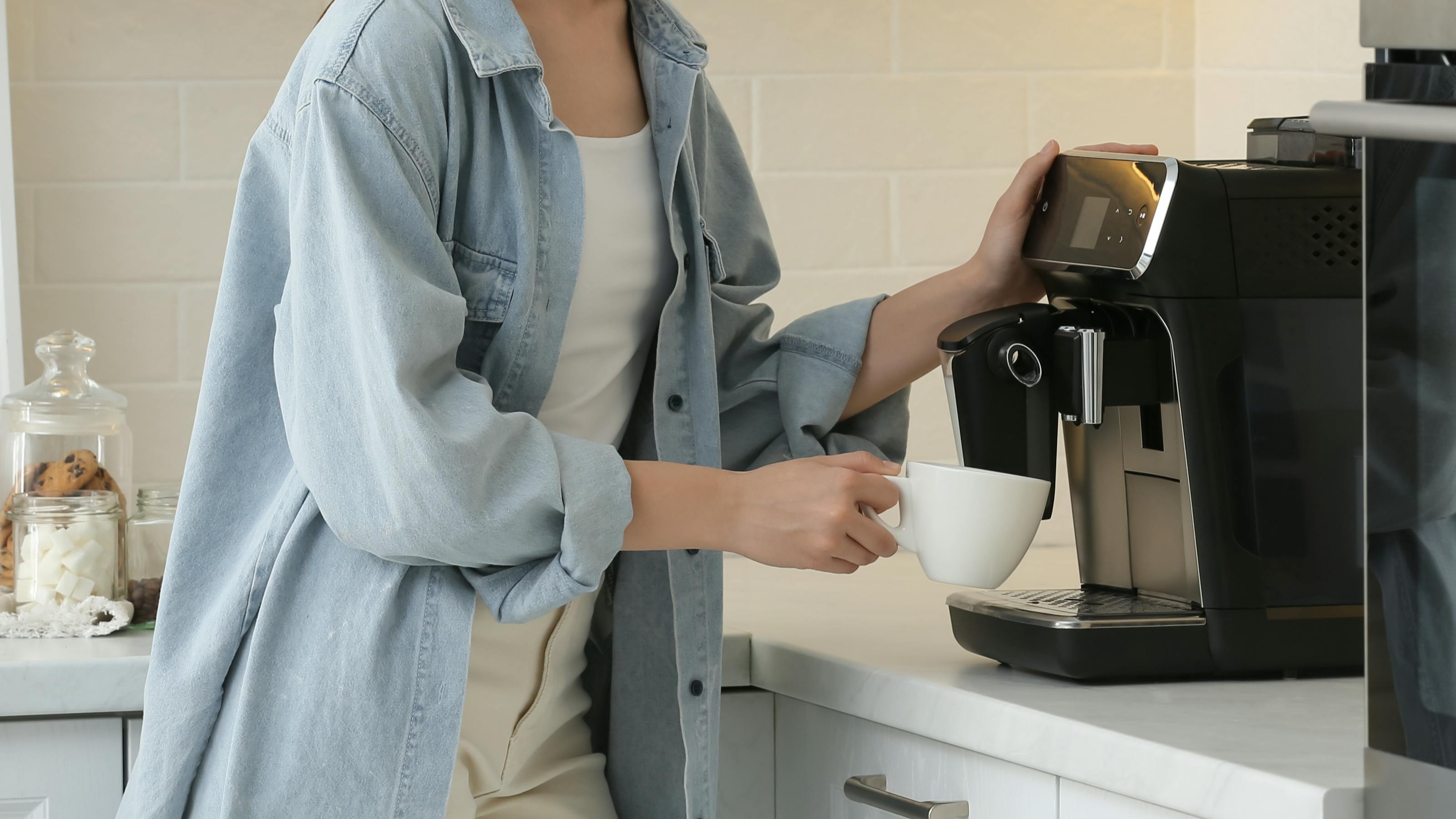 A woman using a coffee grinder on a kitchen counter. 